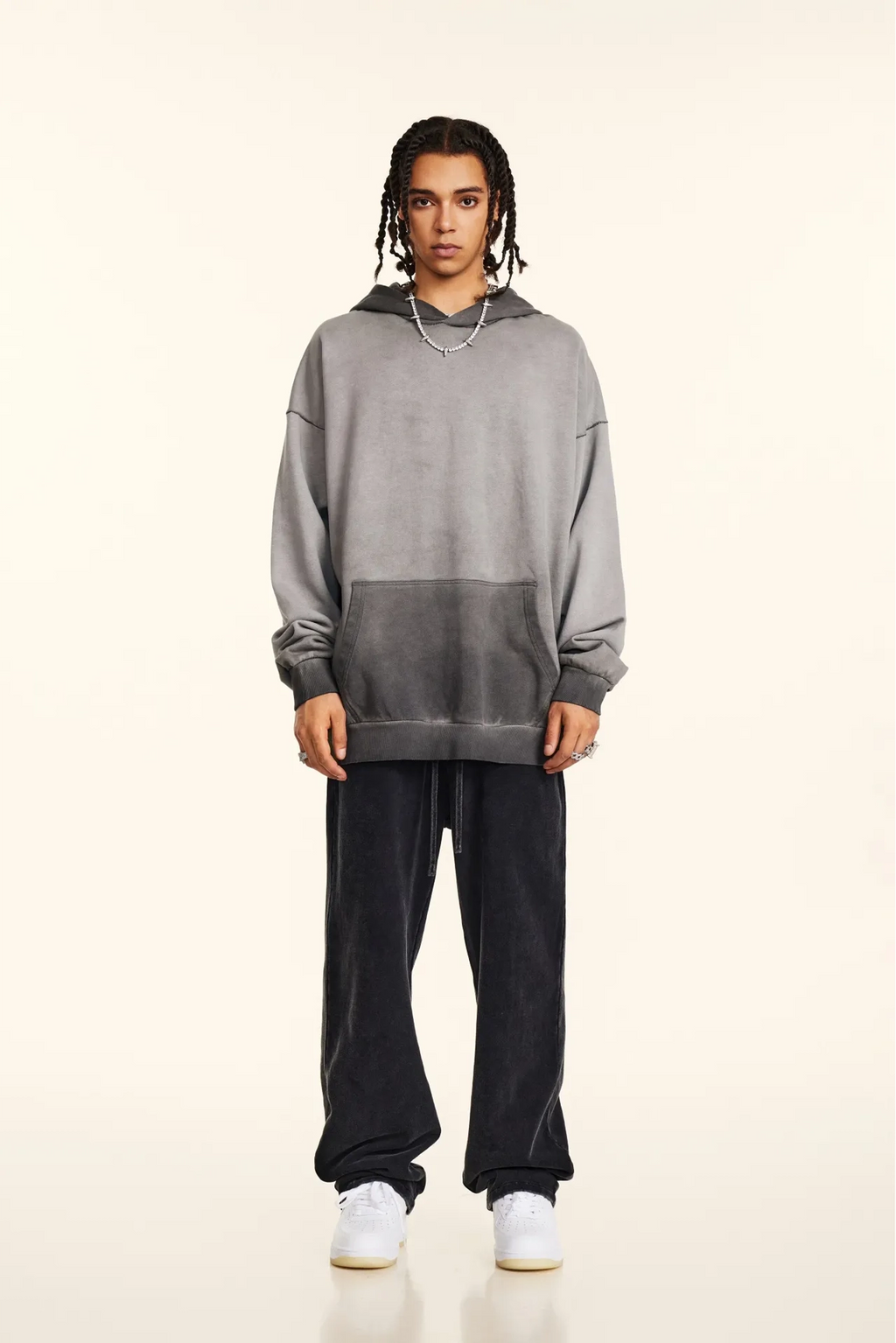 Person wearing a gray hoodie and black pants on a white background