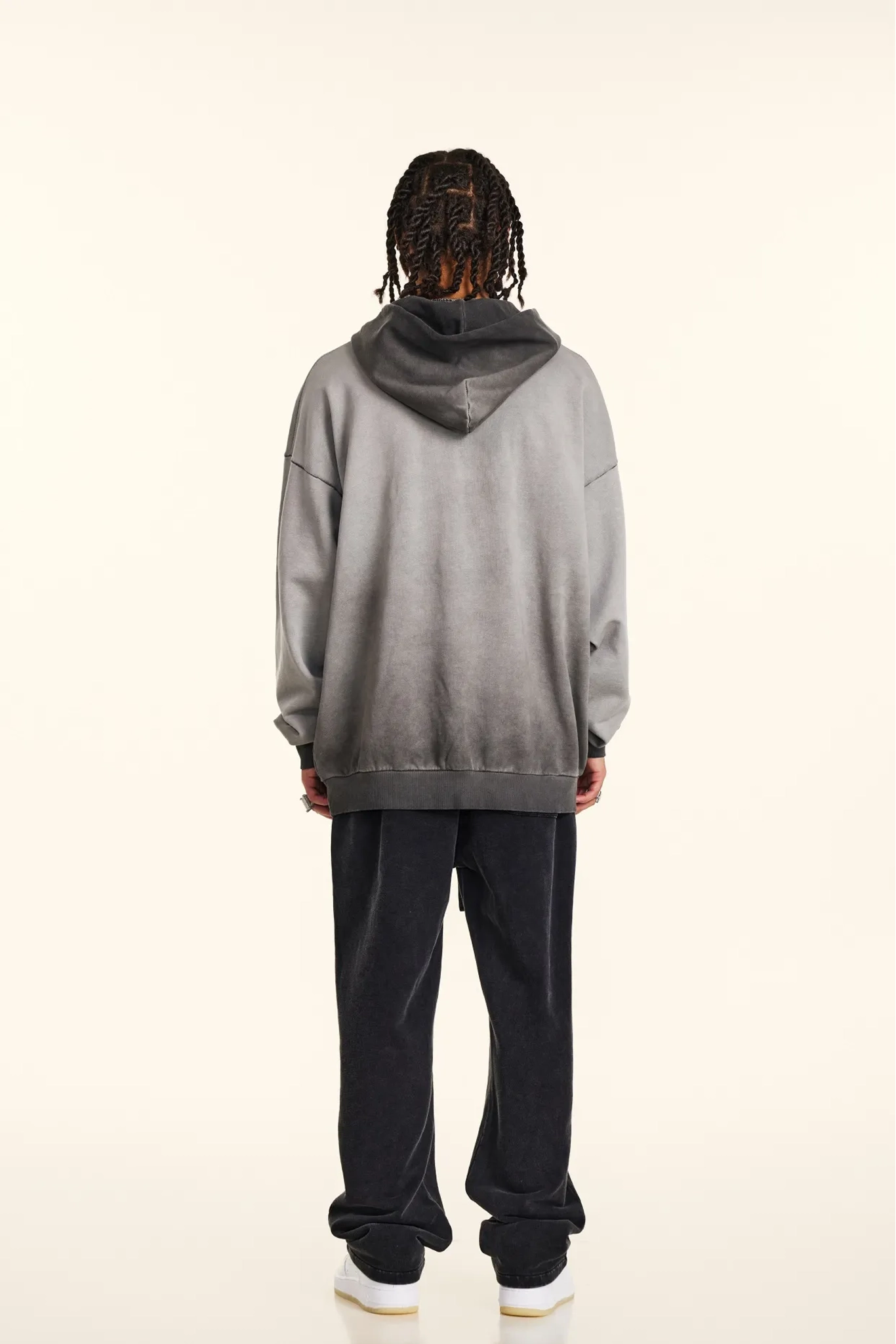 Person wearing a gray hoodie and black pants on a beige background