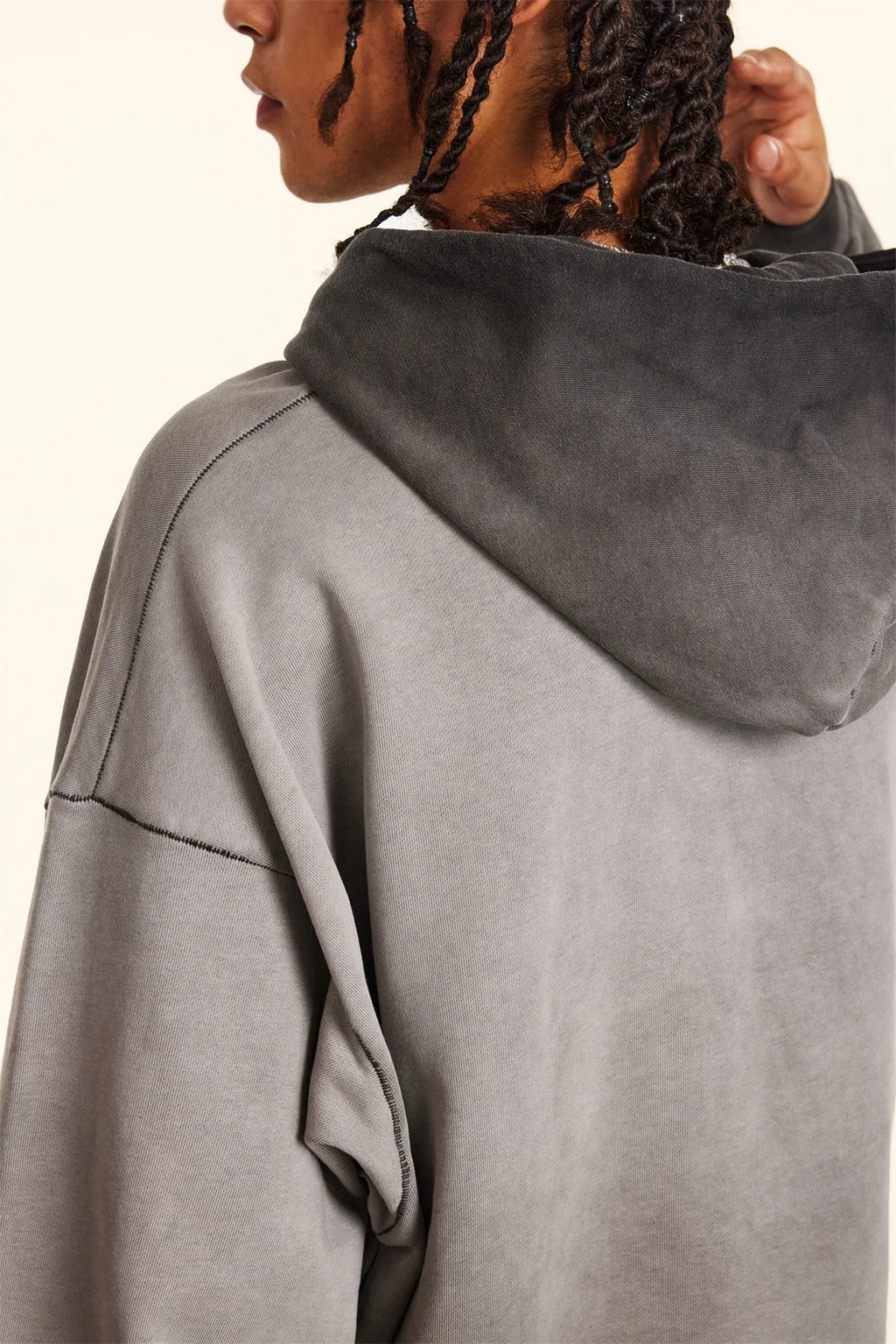 Gray hoodie worn by a person with braided hair on a white background