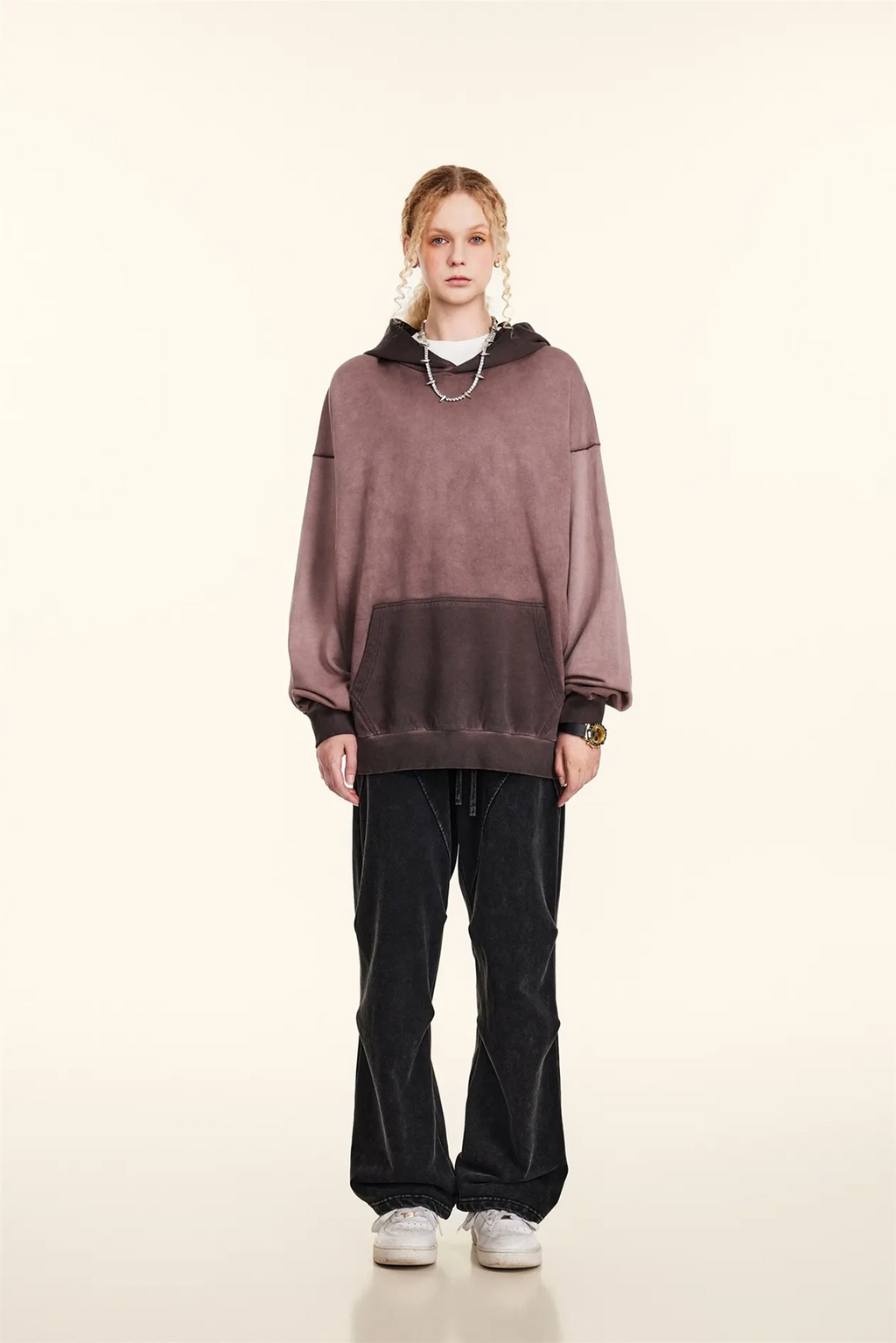 Person wearing a oversized mauve hoodie and black pants on a white background