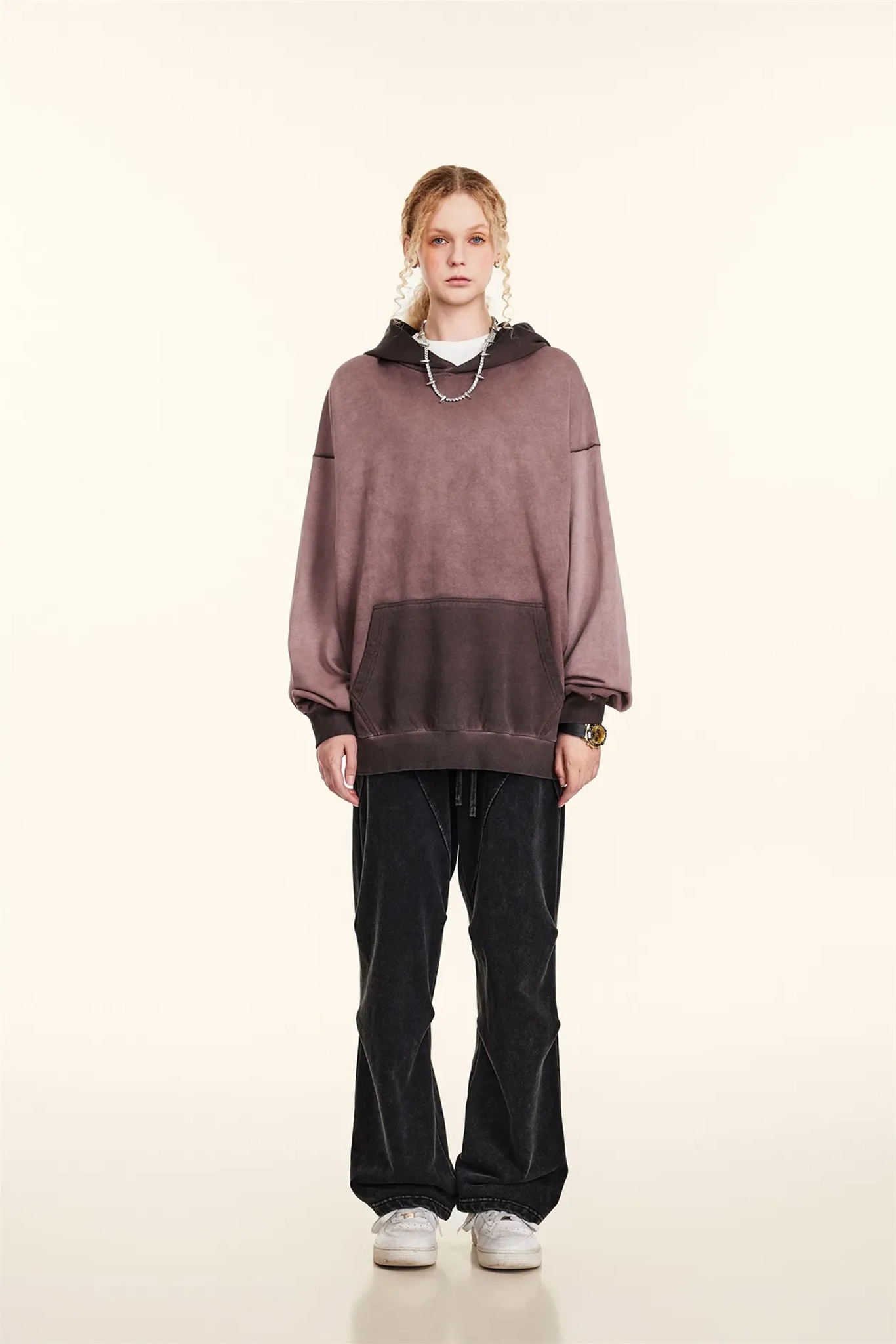 Person wearing a oversized mauve hoodie and black pants on a white background