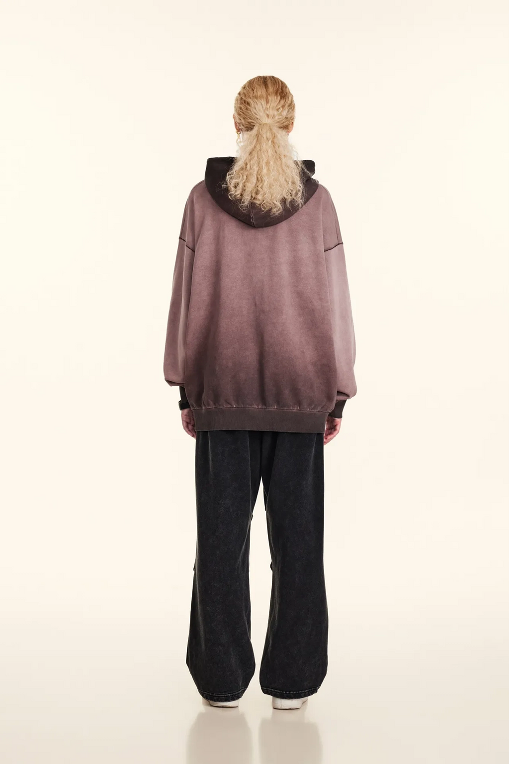 Person wearing a oversized mauve hoodie and black pants on a white background