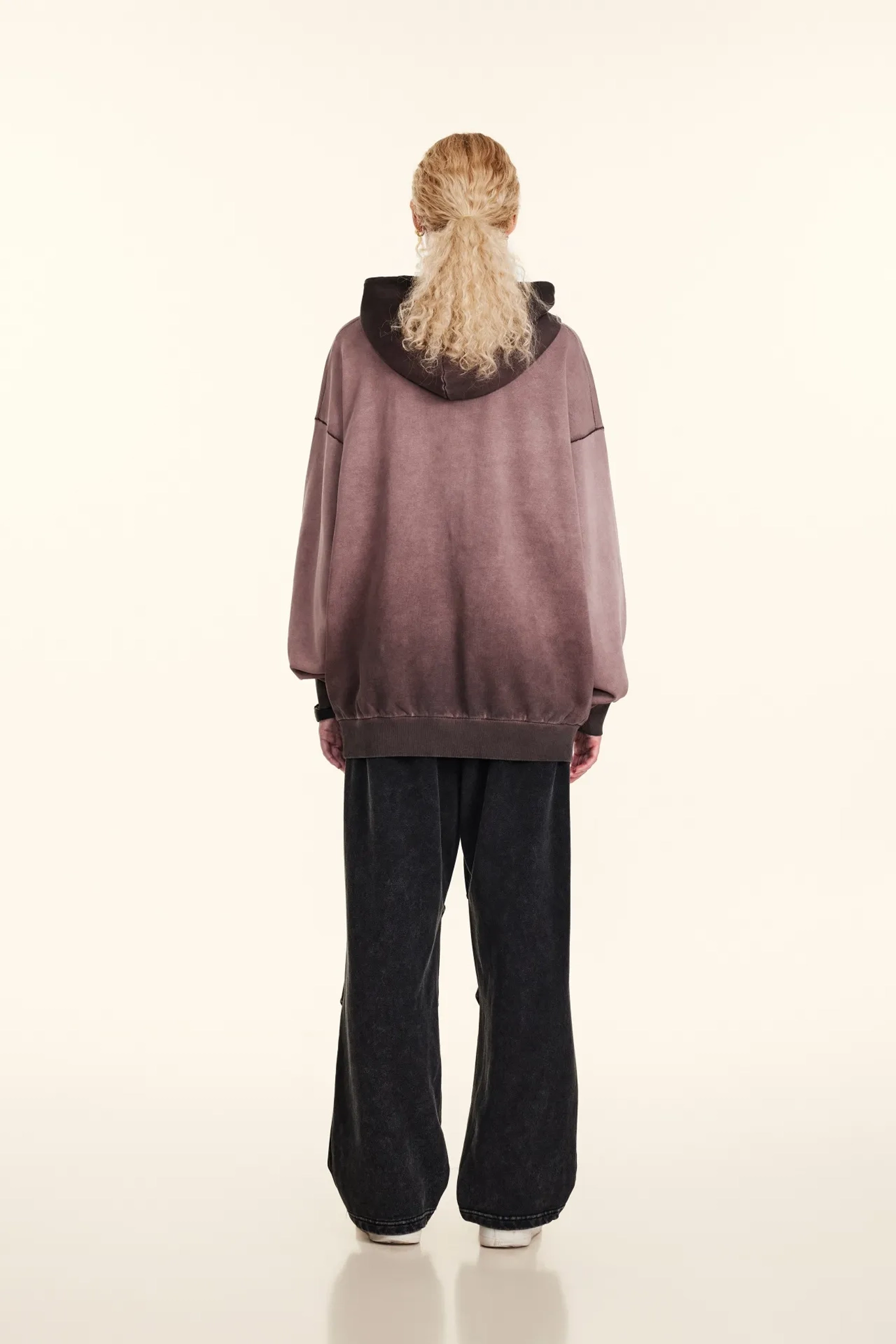 Person wearing a oversized mauve hoodie and black pants on a white background