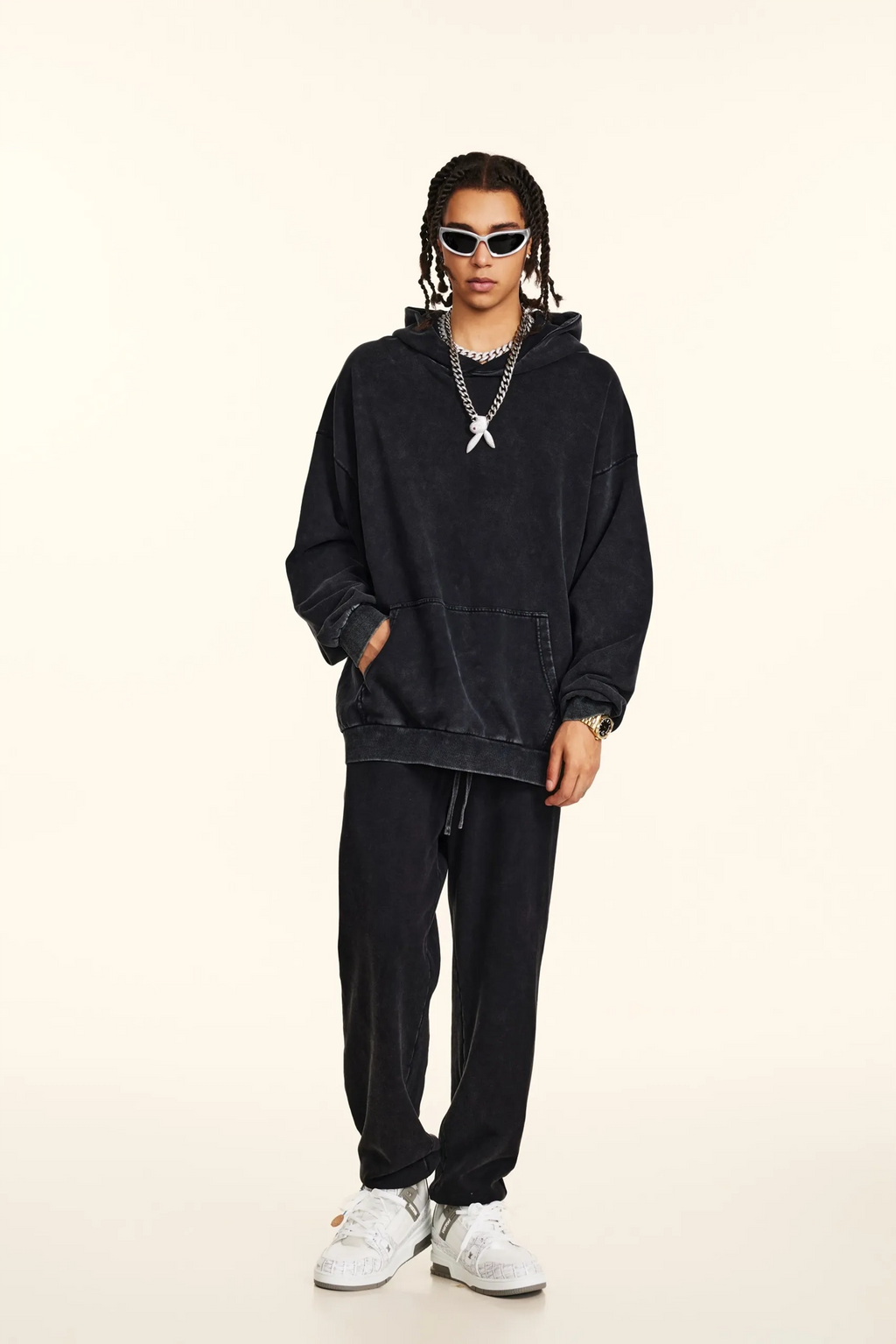 Person wearing a black hoodie and pants with white sneakers on a beige background