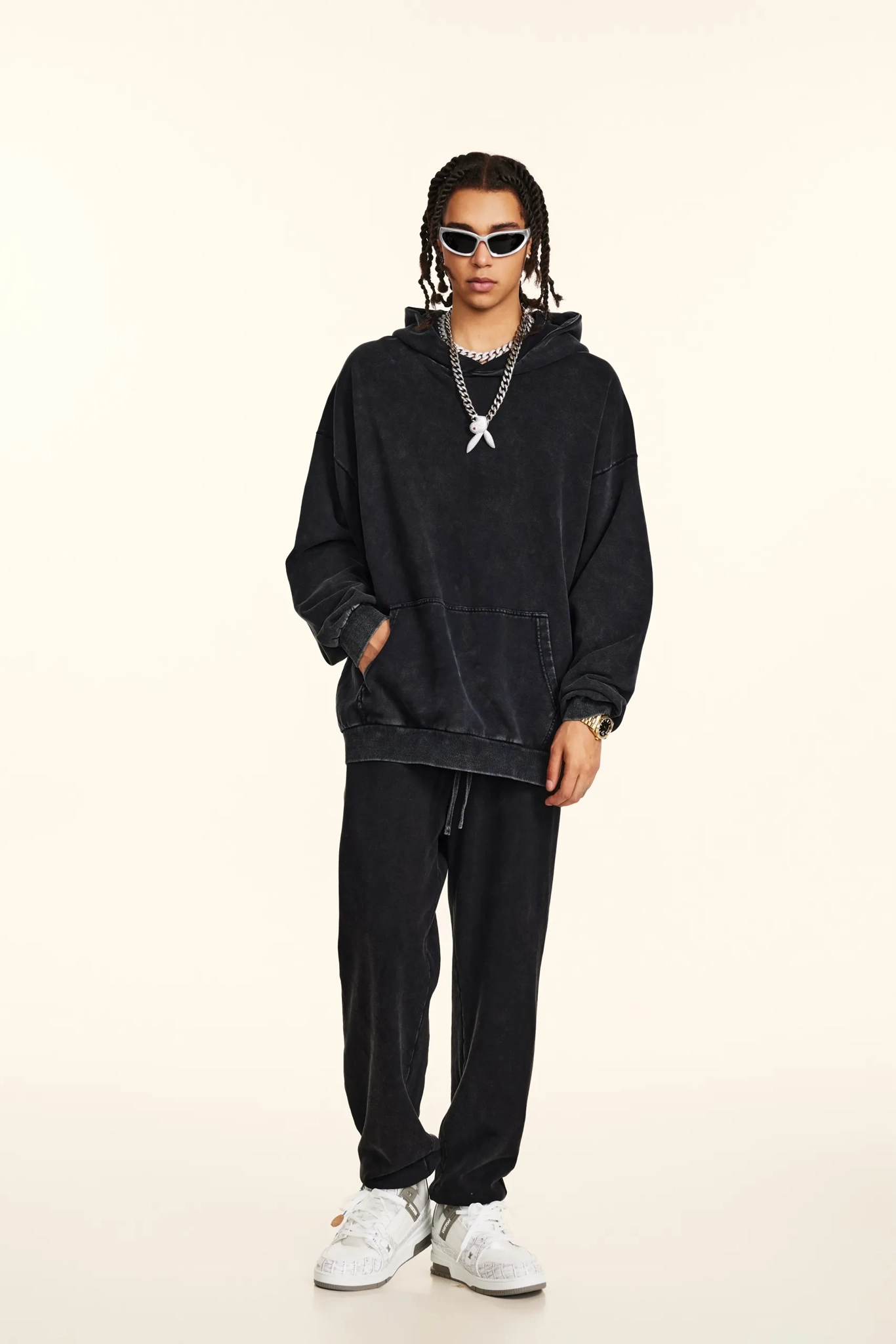 Person wearing a black hoodie and pants with white sneakers on a beige background