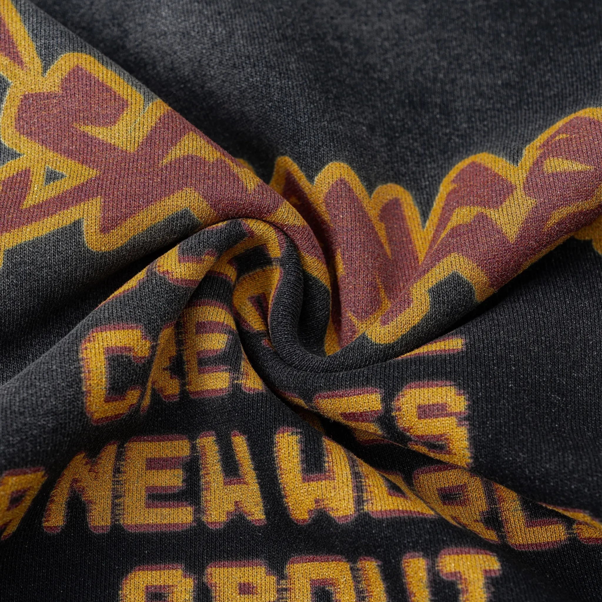 Close-up of fabric with text and pattern, featuring maroon and yellow colors on a black background.
