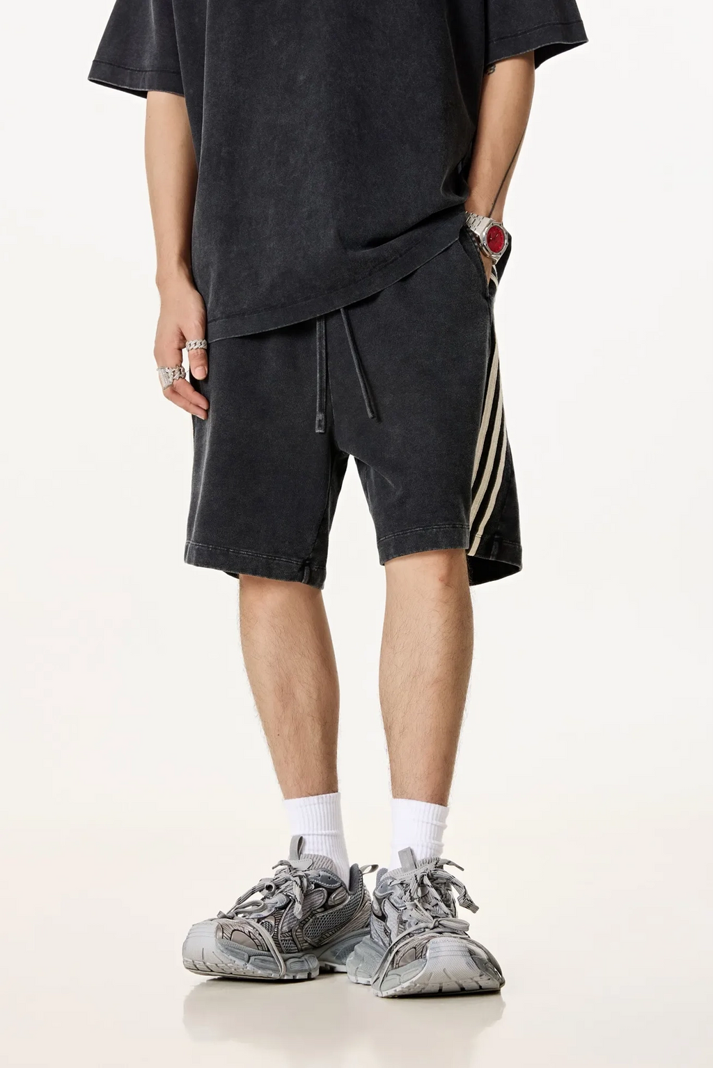 Person wearing black shorts with a brand logo, black t-shirt, and gray sneakers on a white background