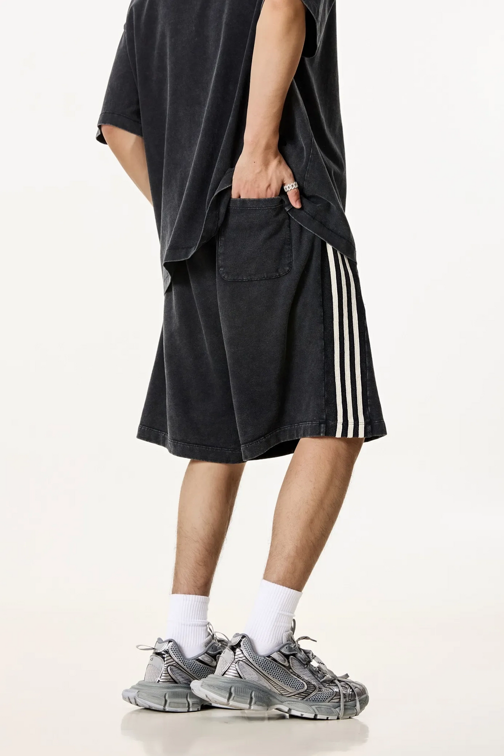 Person wearing black shorts with white stripes, a black oversized shirt, and gray sneakers on a white background