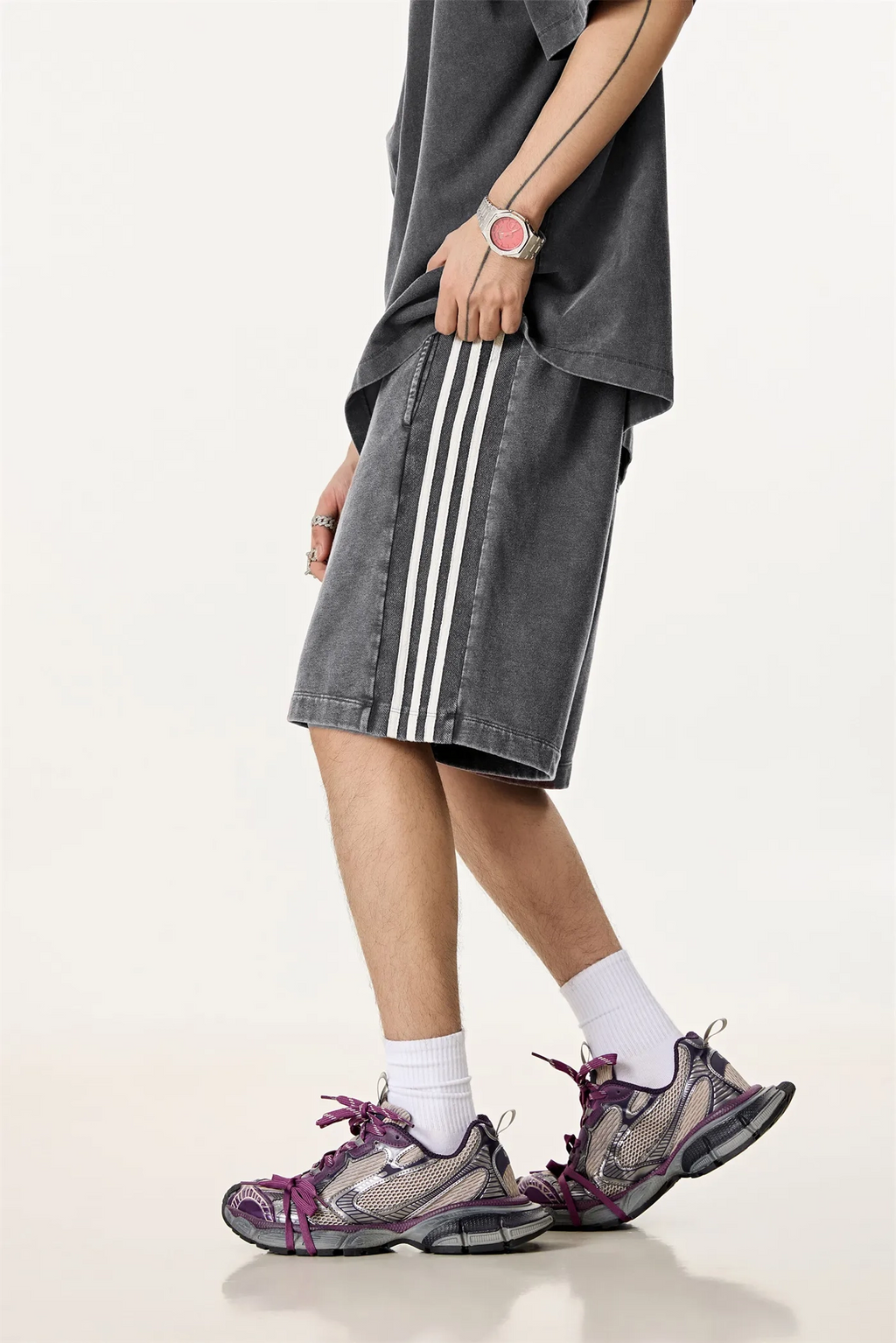 Person wearing gray shorts with white stripes, a dark shirt, and purple sneakers on a light background