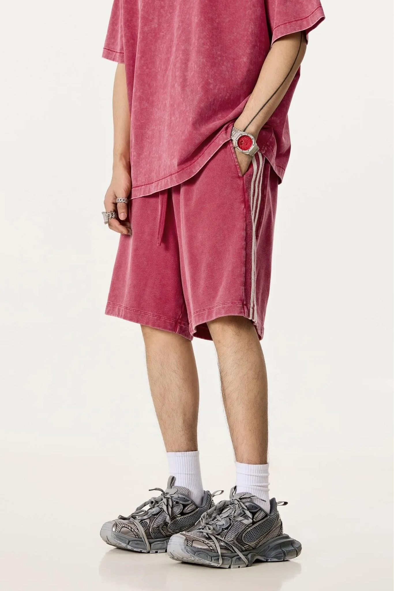 Person wearing a red oversized t-shirt and shorts with white socks and gray sneakers on a white background