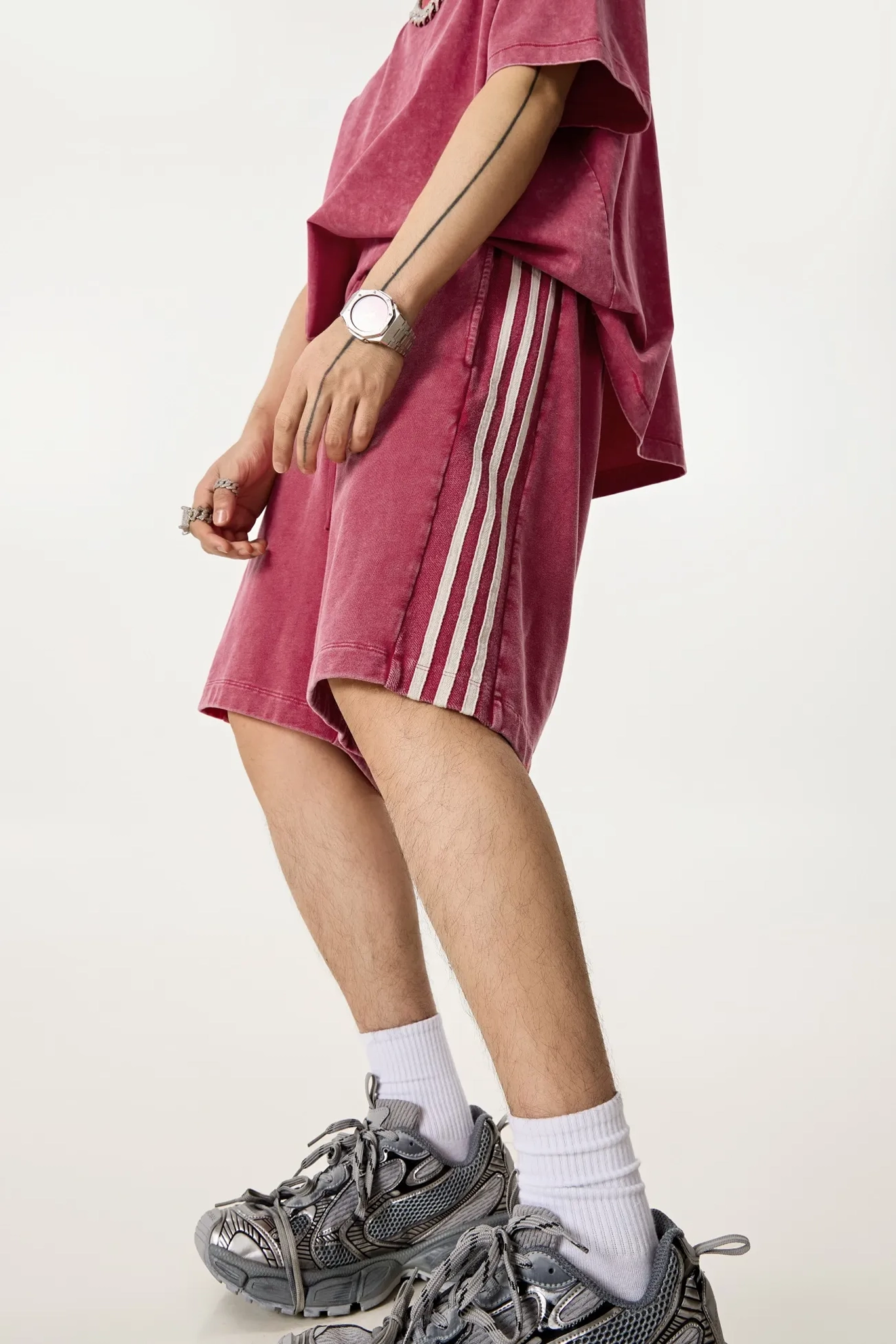 Person wearing a maroon Adidas skirt with white stripes, maroon top, and gray sneakers on a light background