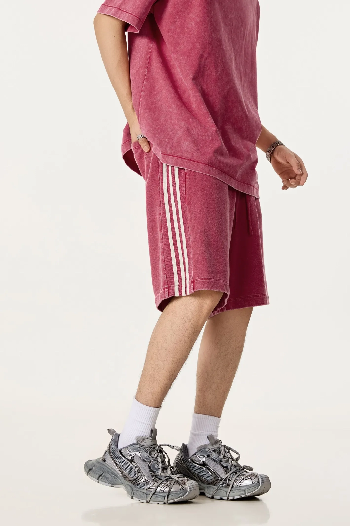Person wearing a pink oversized t-shirt and shorts with white stripes, paired with gray sneakers on a white background.