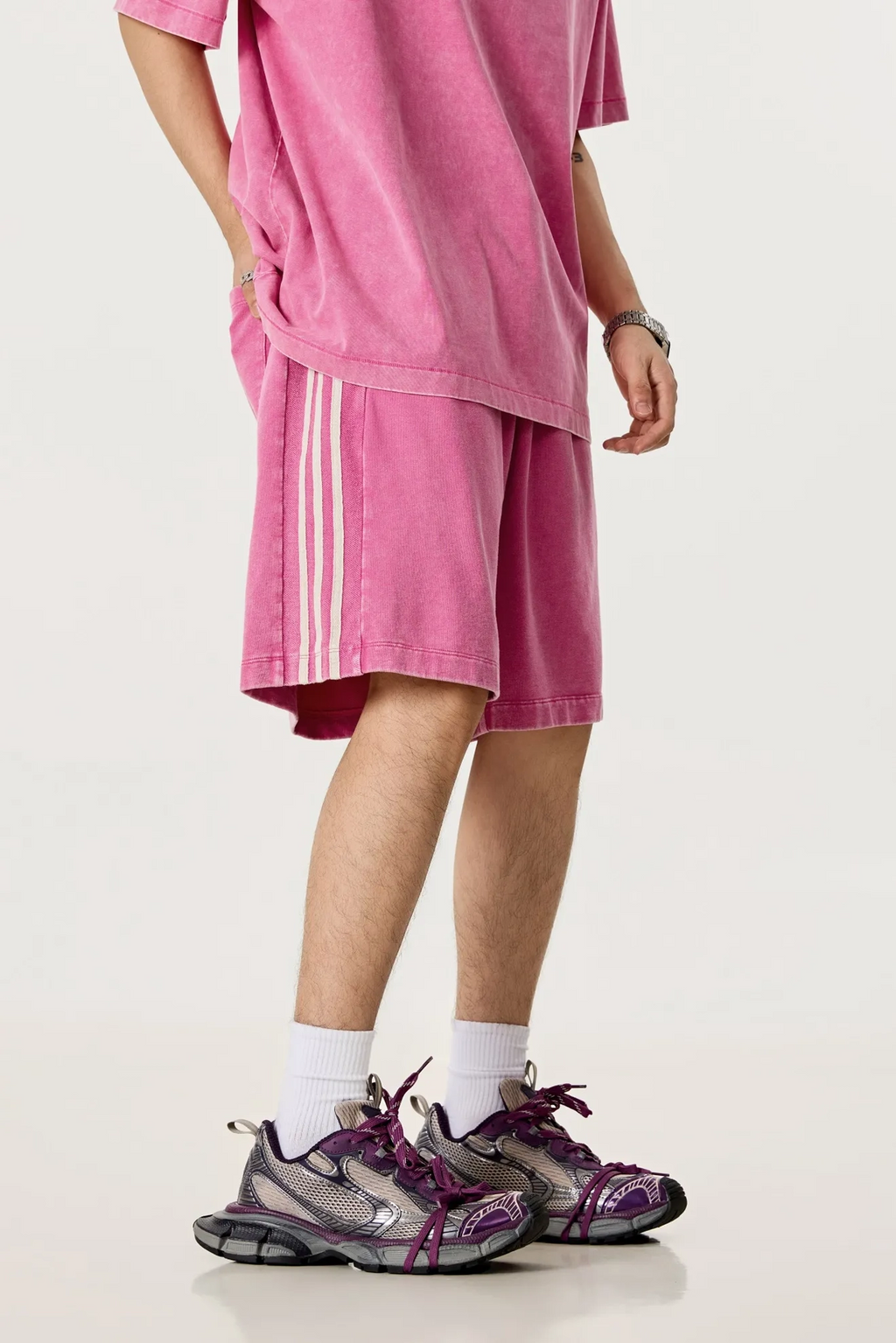 Person wearing pink shorts and a matching shirt with white socks and purple shoes on a white background