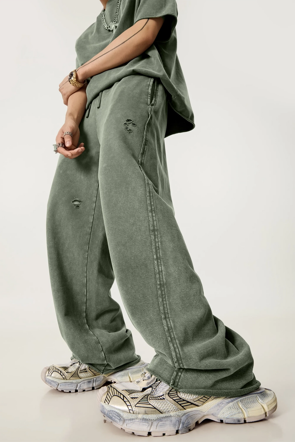 Person wearing a loose-fitting green outfit with wide-leg pants and chunky shoes on a plain background