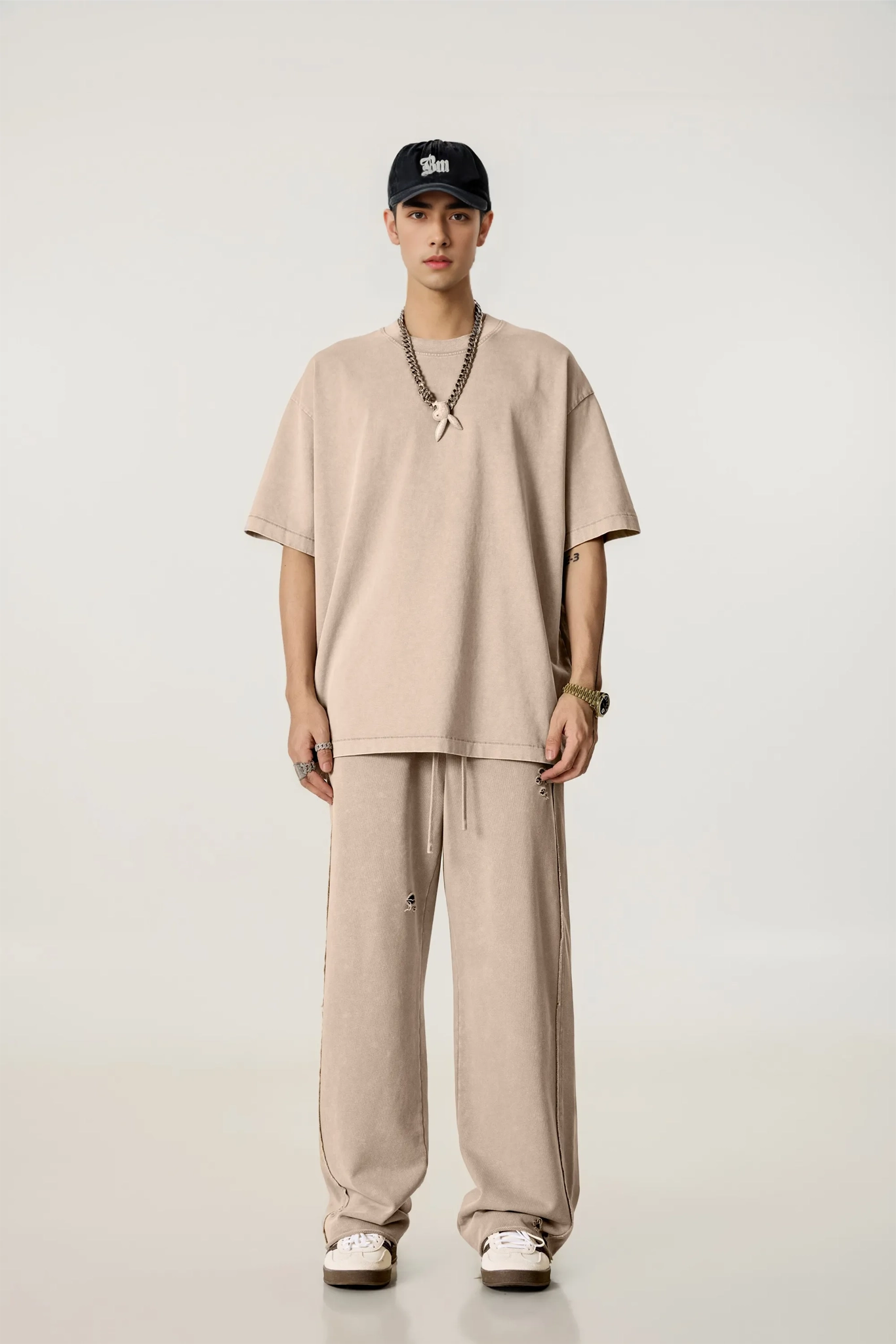 Person wearing a beige outfit with a cap on a white background