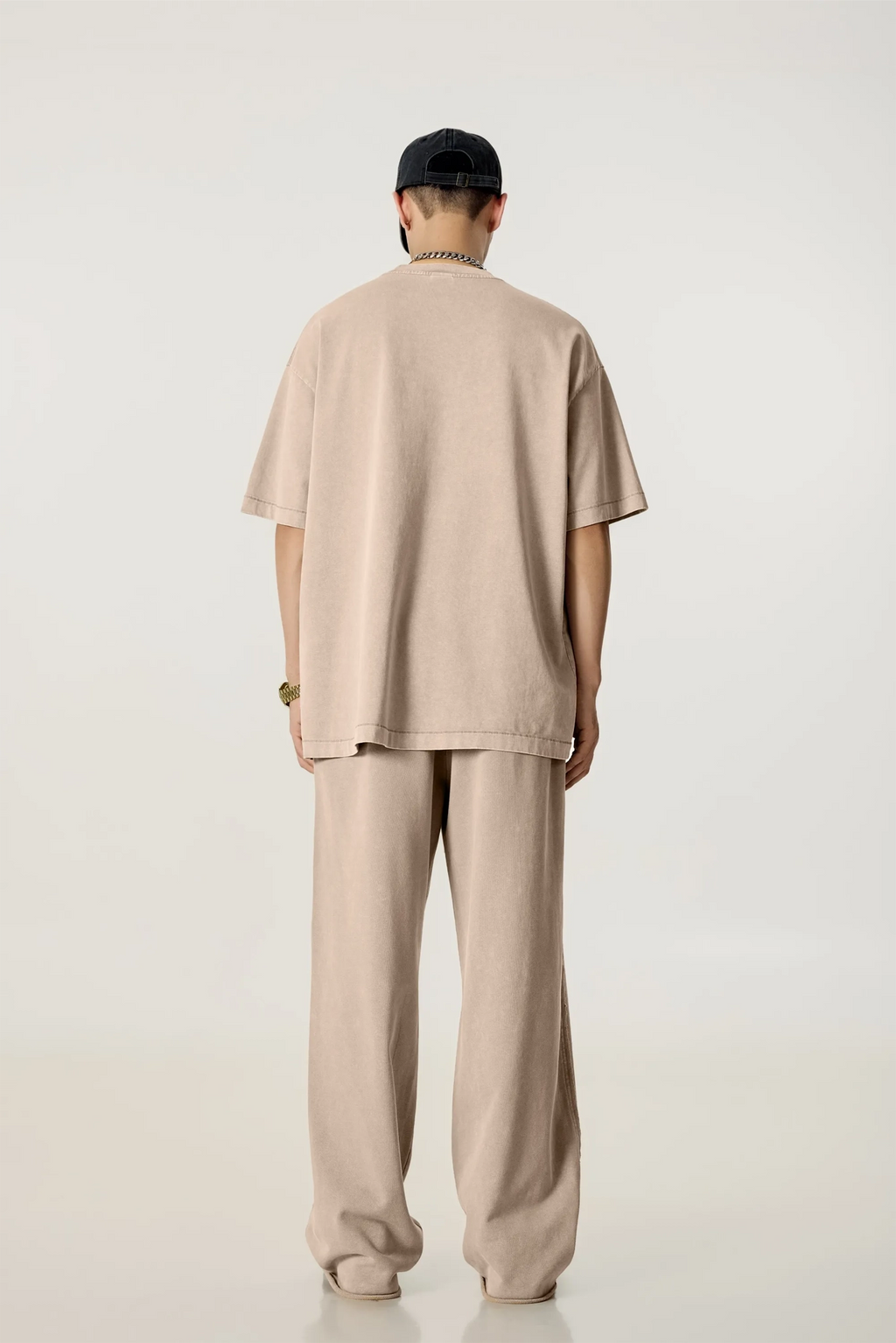 Person wearing a beige outfit with a cap on a white background