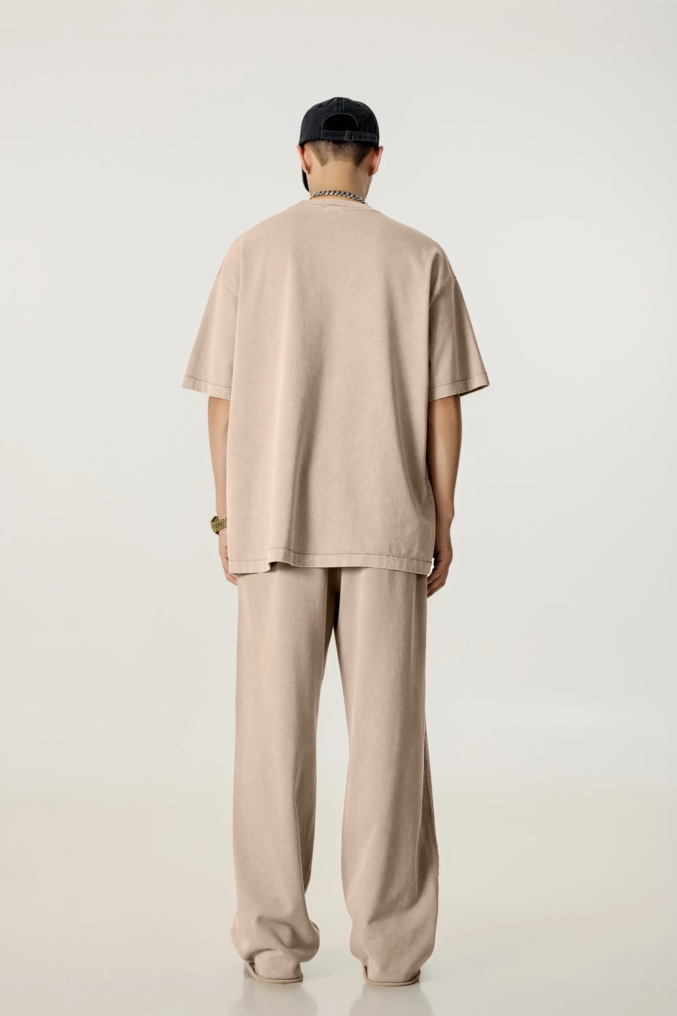 Person wearing a beige outfit with a cap on a white background