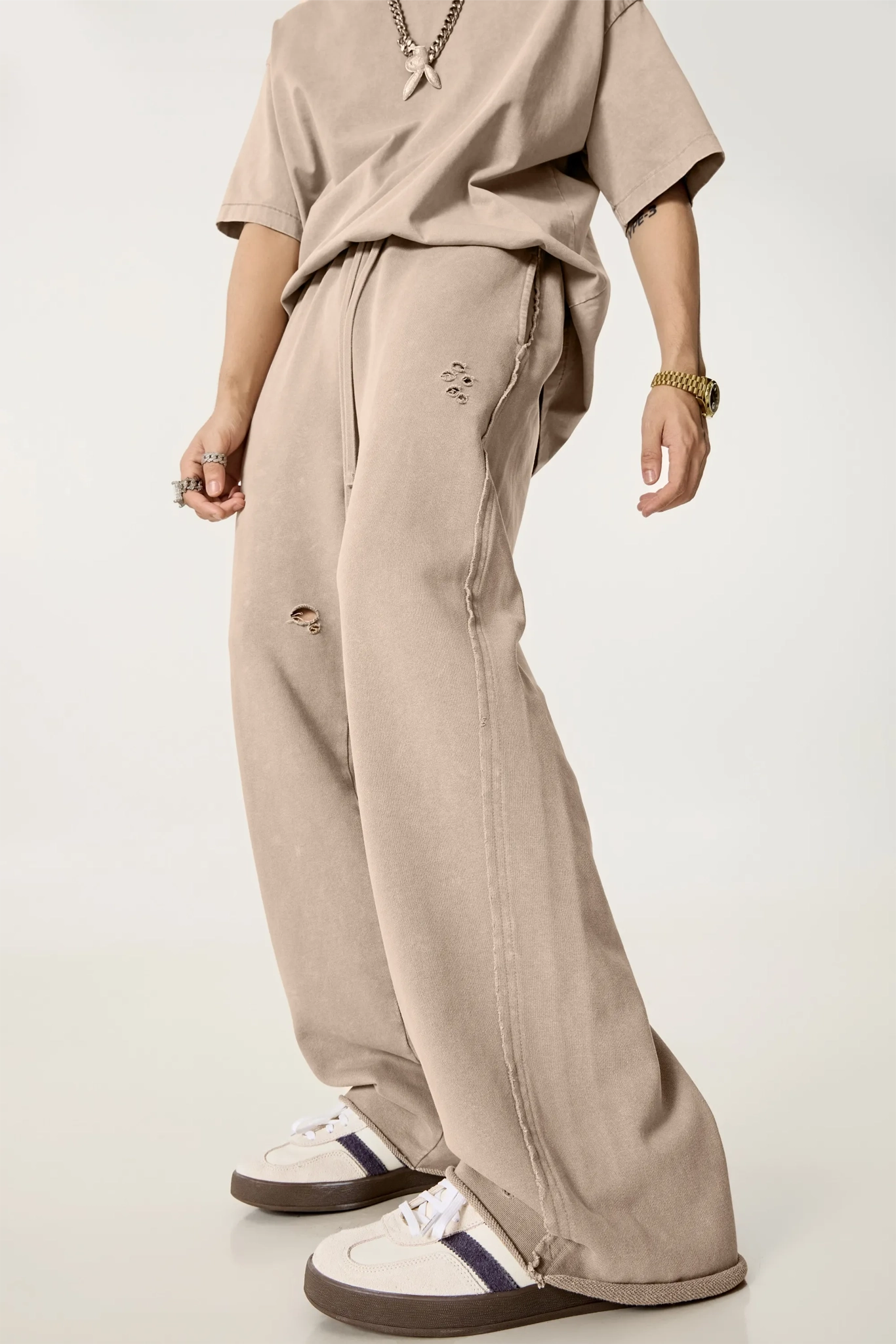 Person wearing a beige outfit with wide-leg pants and white sneakers on a light background