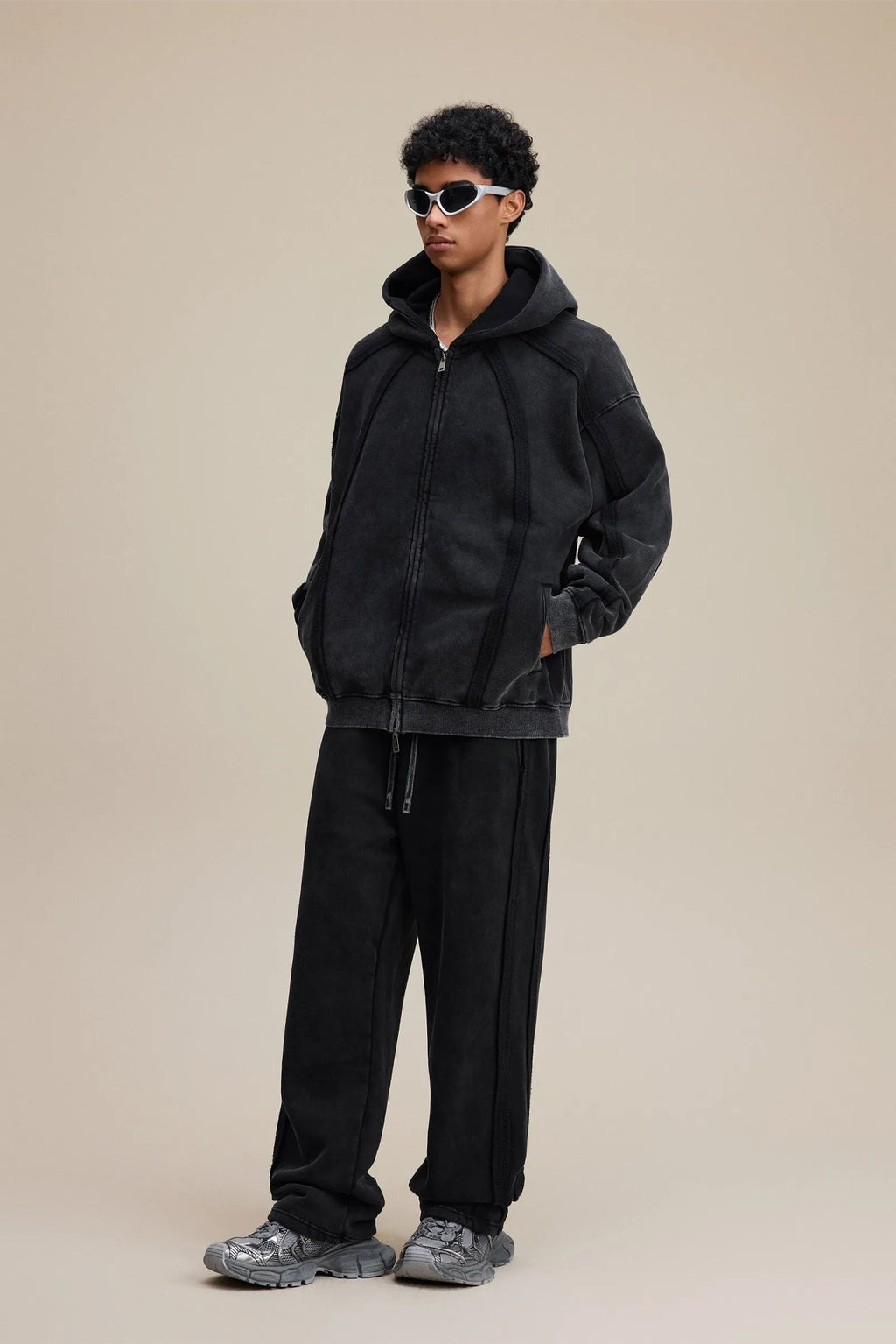 Person wearing a black tracksuit with sunglasses on a beige background