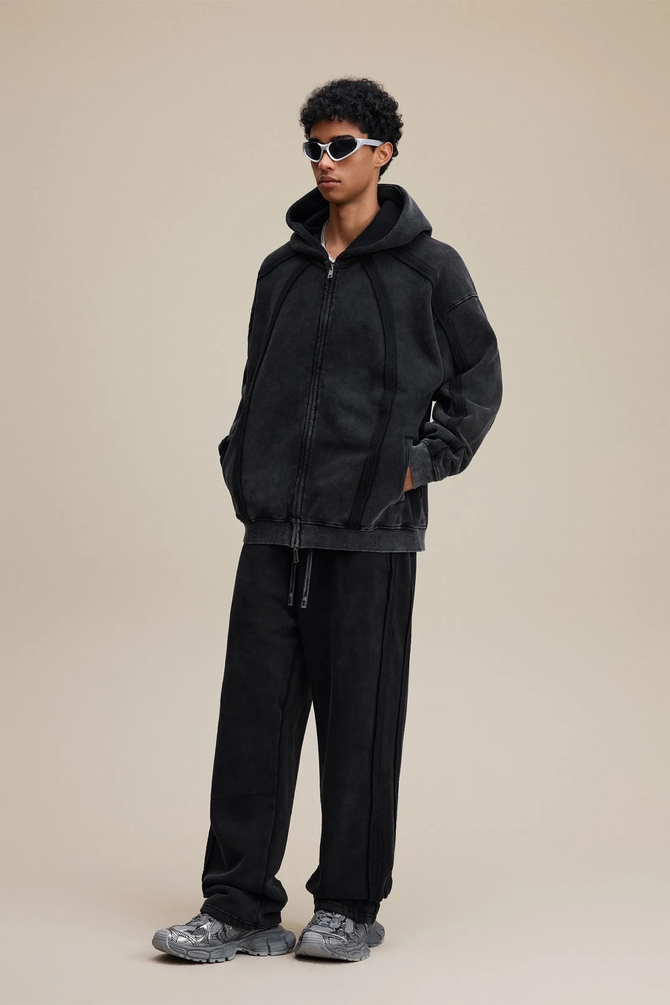 Person wearing a black tracksuit with sunglasses on a beige background