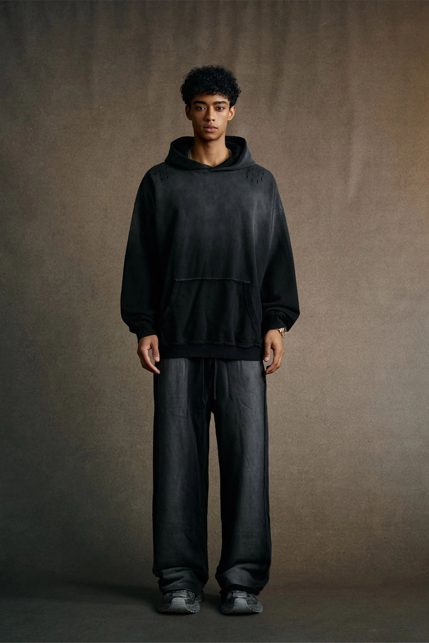 Person wearing a black hoodie and pants against a brown background