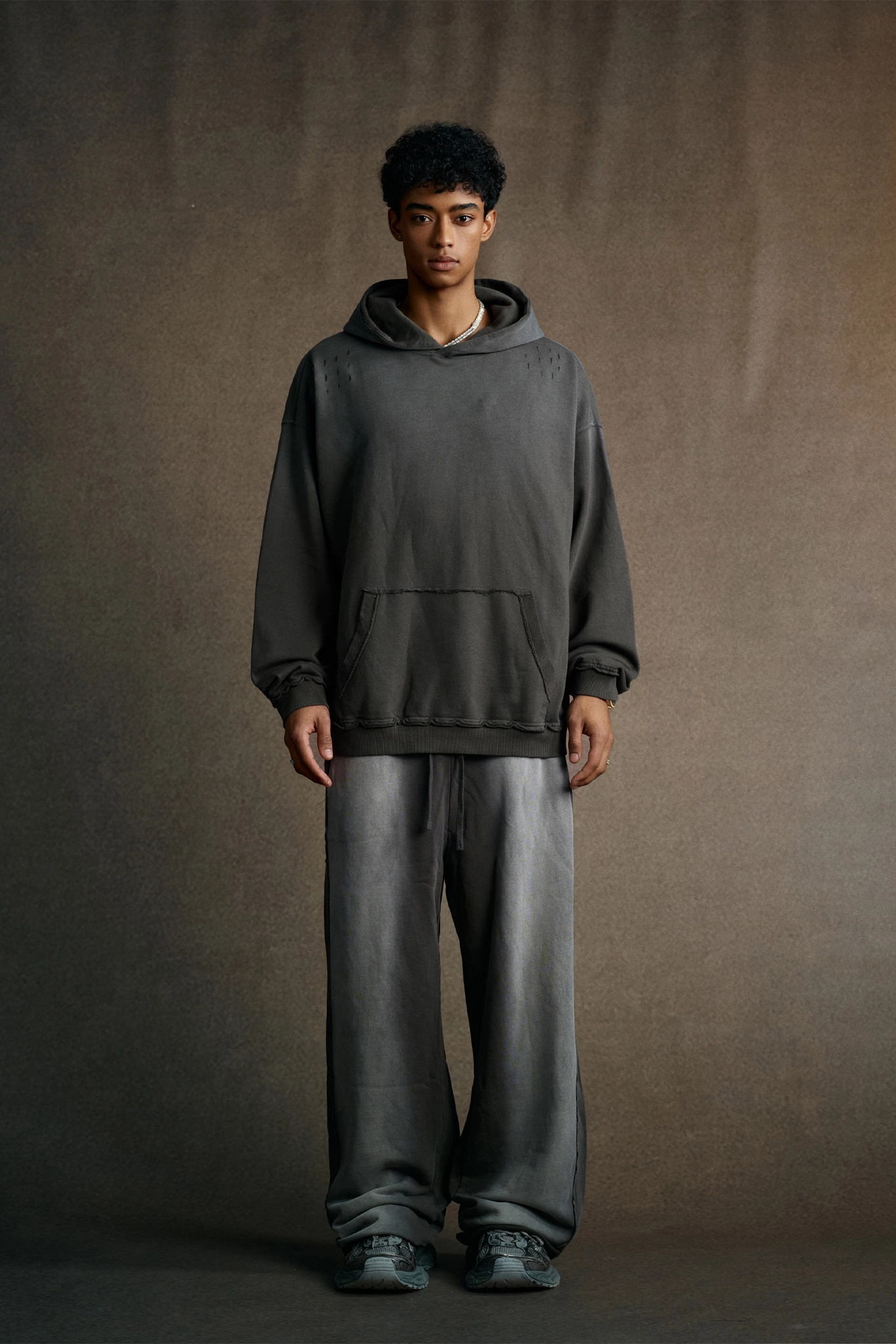 Person wearing a dark gray hoodie and pants against a brown background