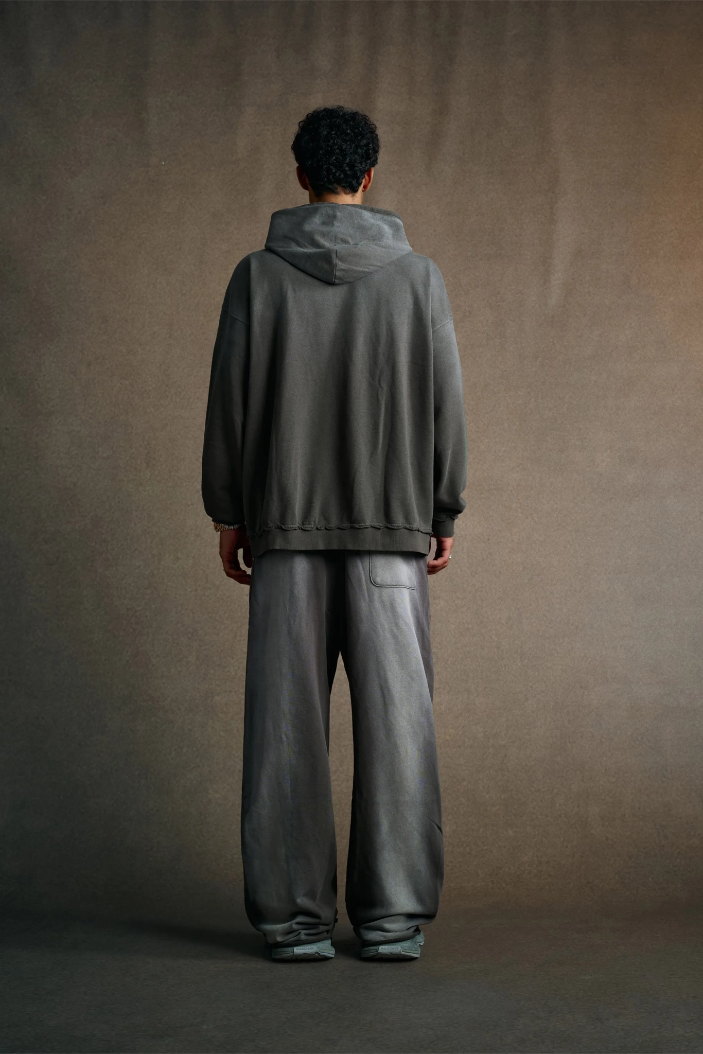 Person wearing a gray hoodie and pants standing against a plain background
