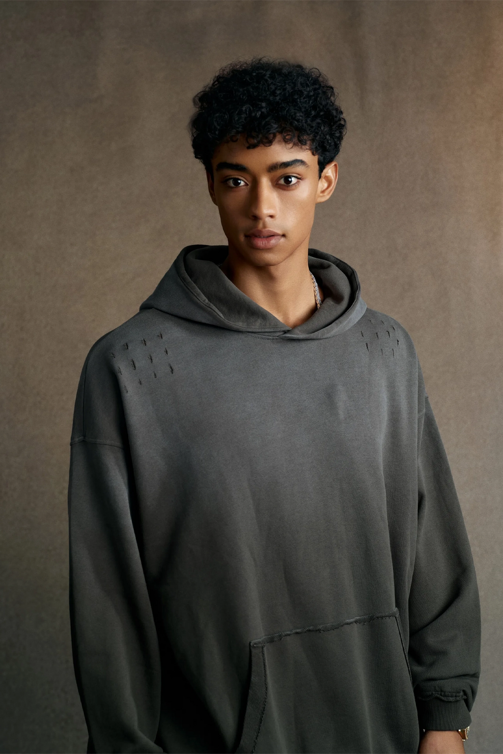 Person wearing a gray hoodie against a brown background