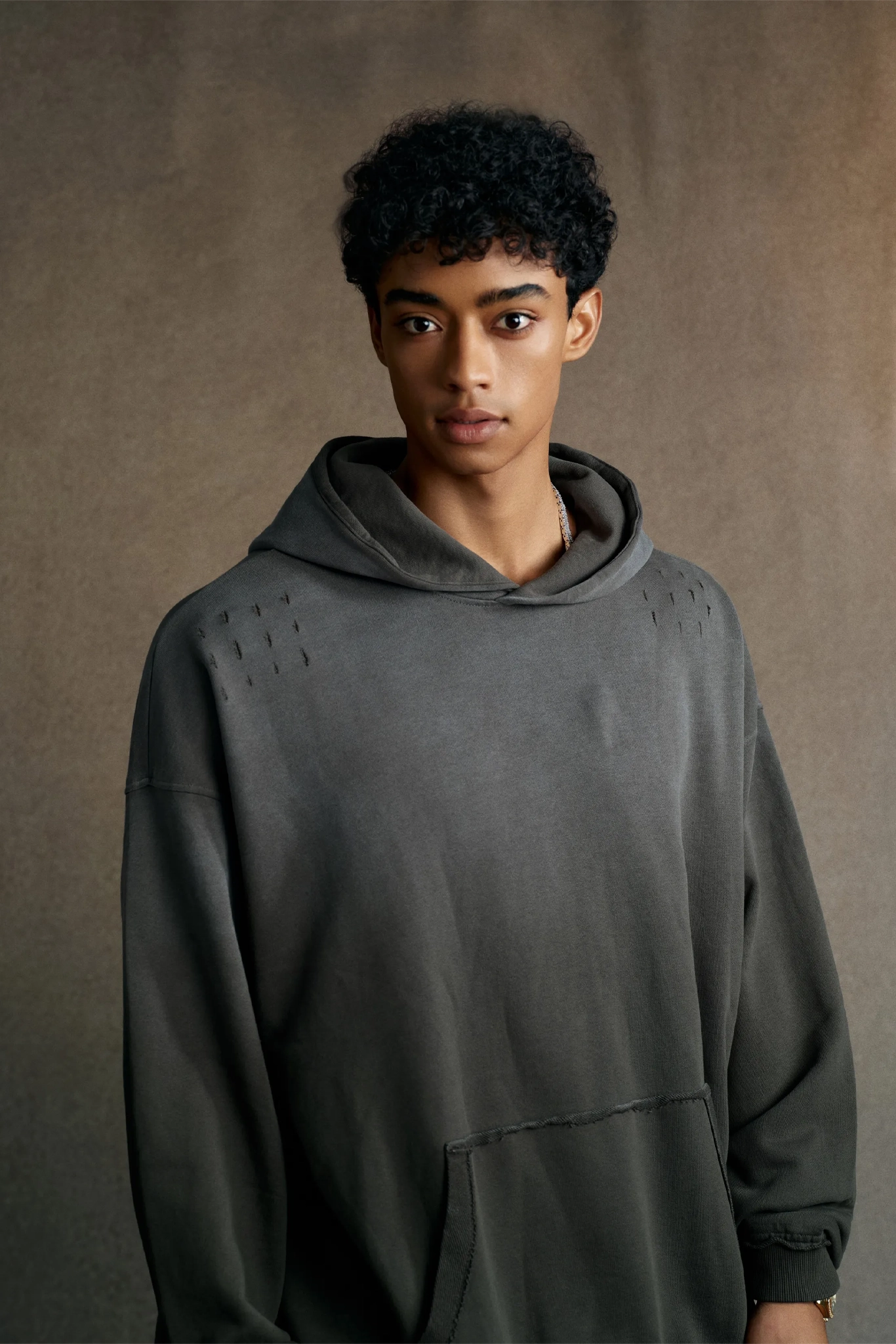 Person wearing a gray hoodie against a brown background