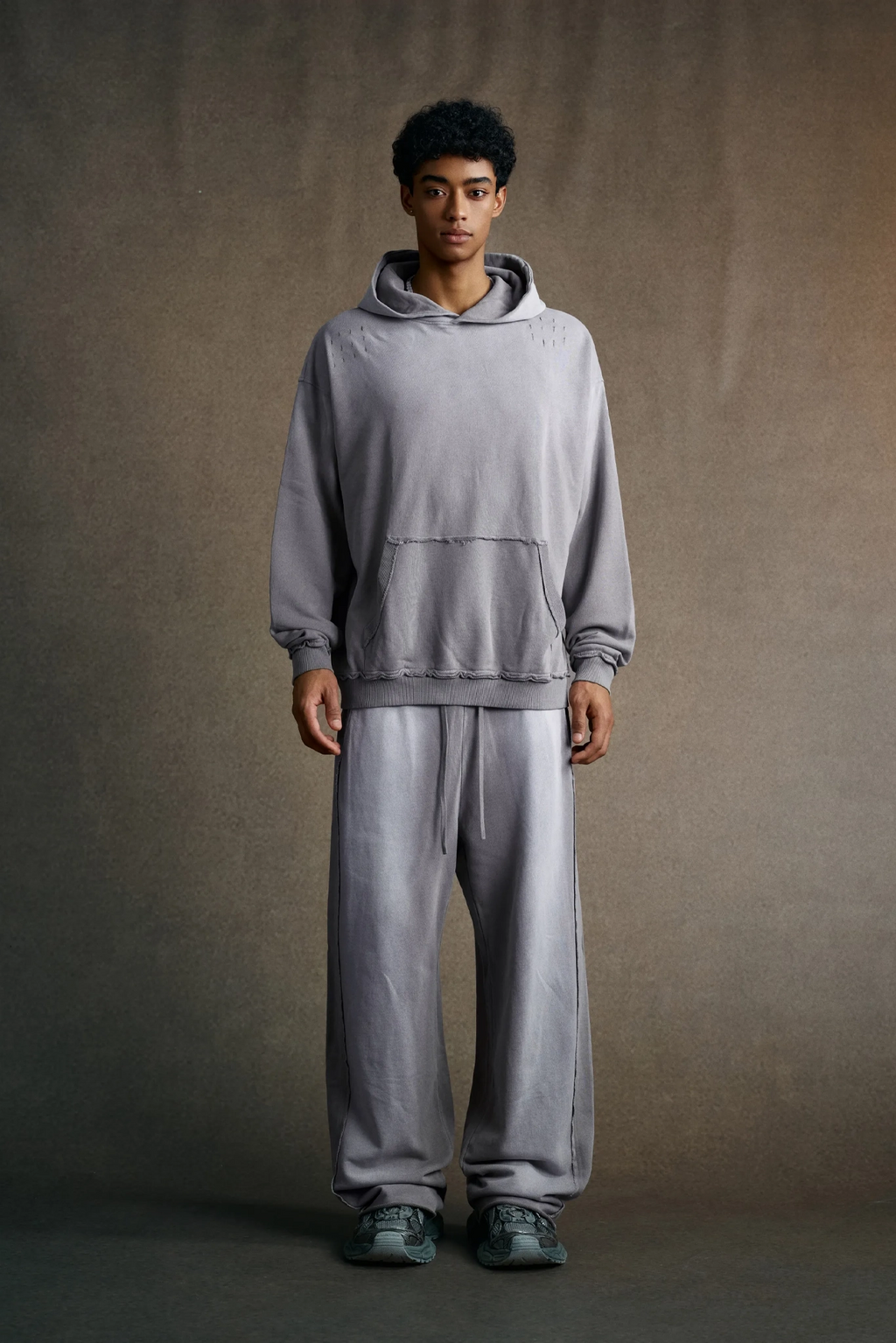 Person wearing a gray hoodie and pants against a plain background