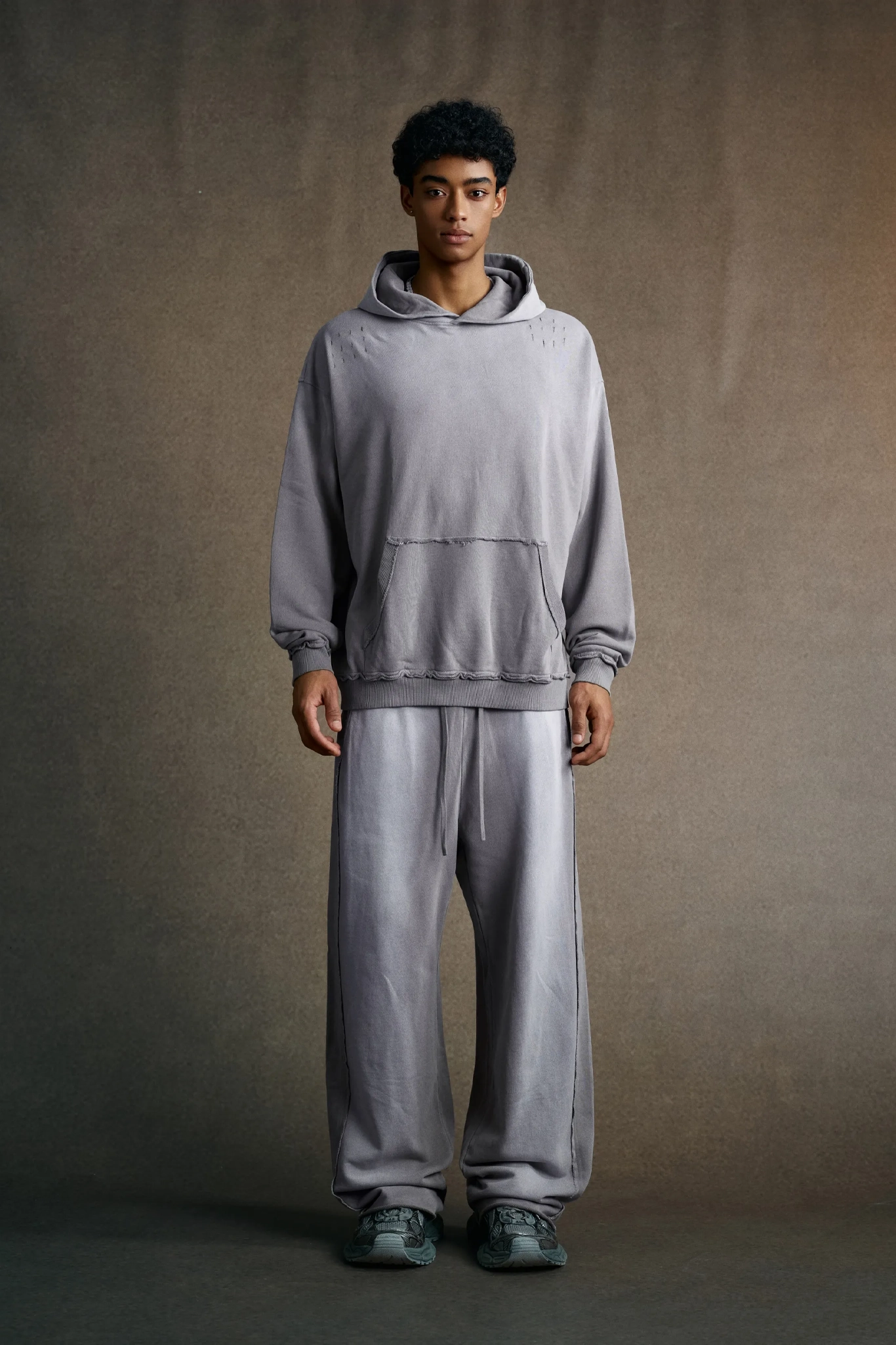 Person wearing a gray hoodie and pants against a plain background