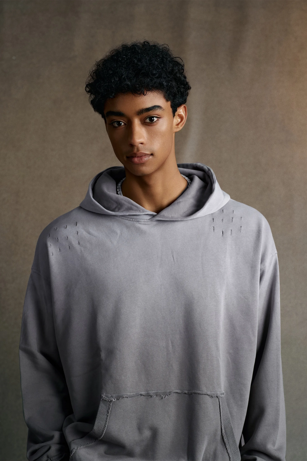 Person wearing a gray hoodie against a brown background