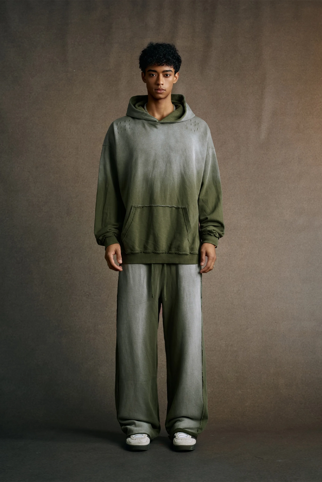 Person wearing a green gradient hoodie and pants against a brown background