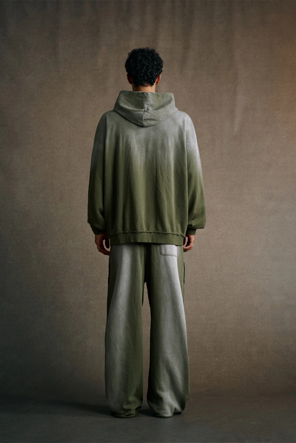 Person wearing a green hoodie and gray pants against a brown background