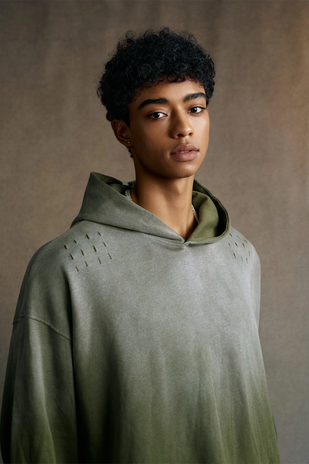 Person wearing a green hooded garment against a brown background