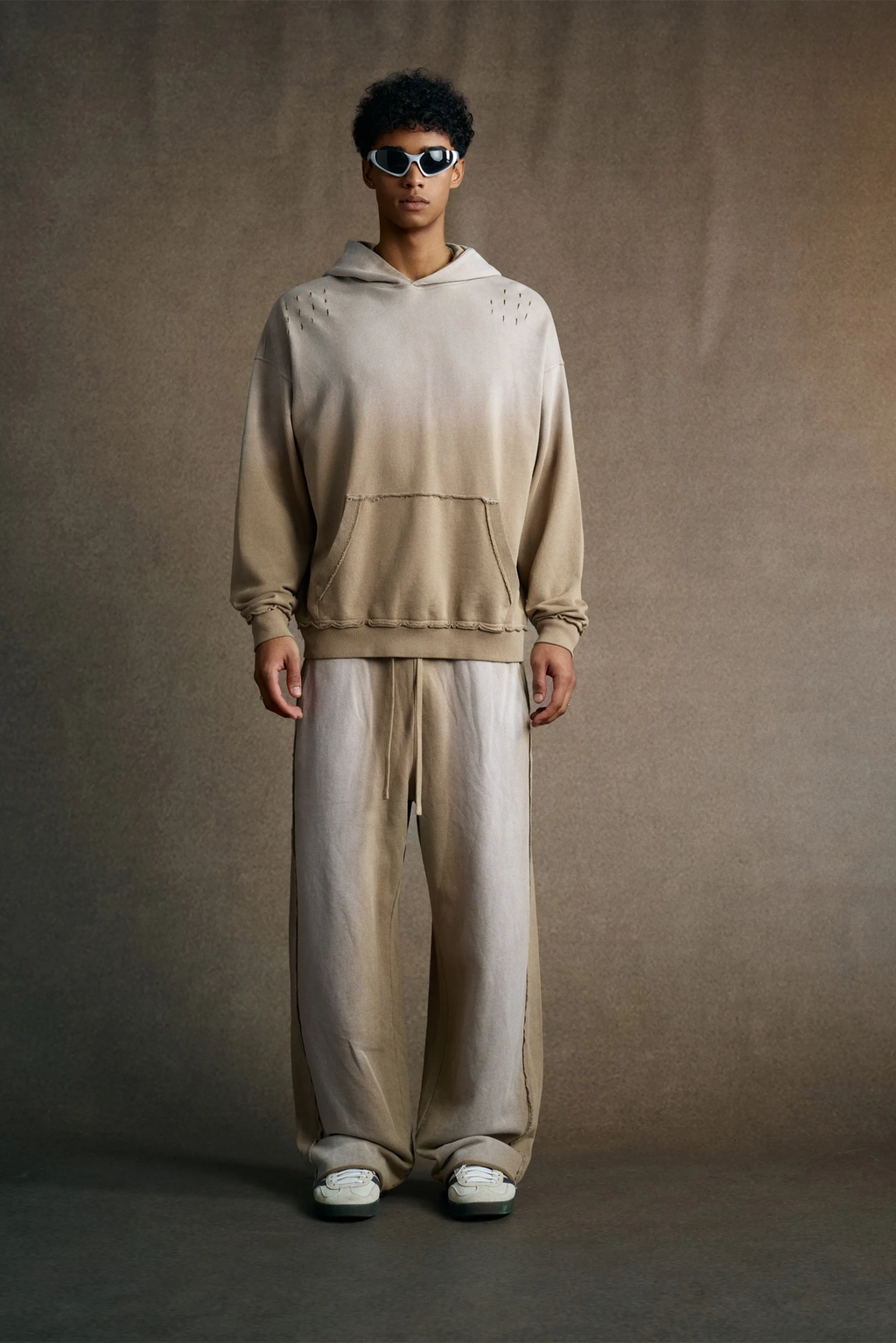 Person wearing a beige gradient hoodie and pants against a brown background