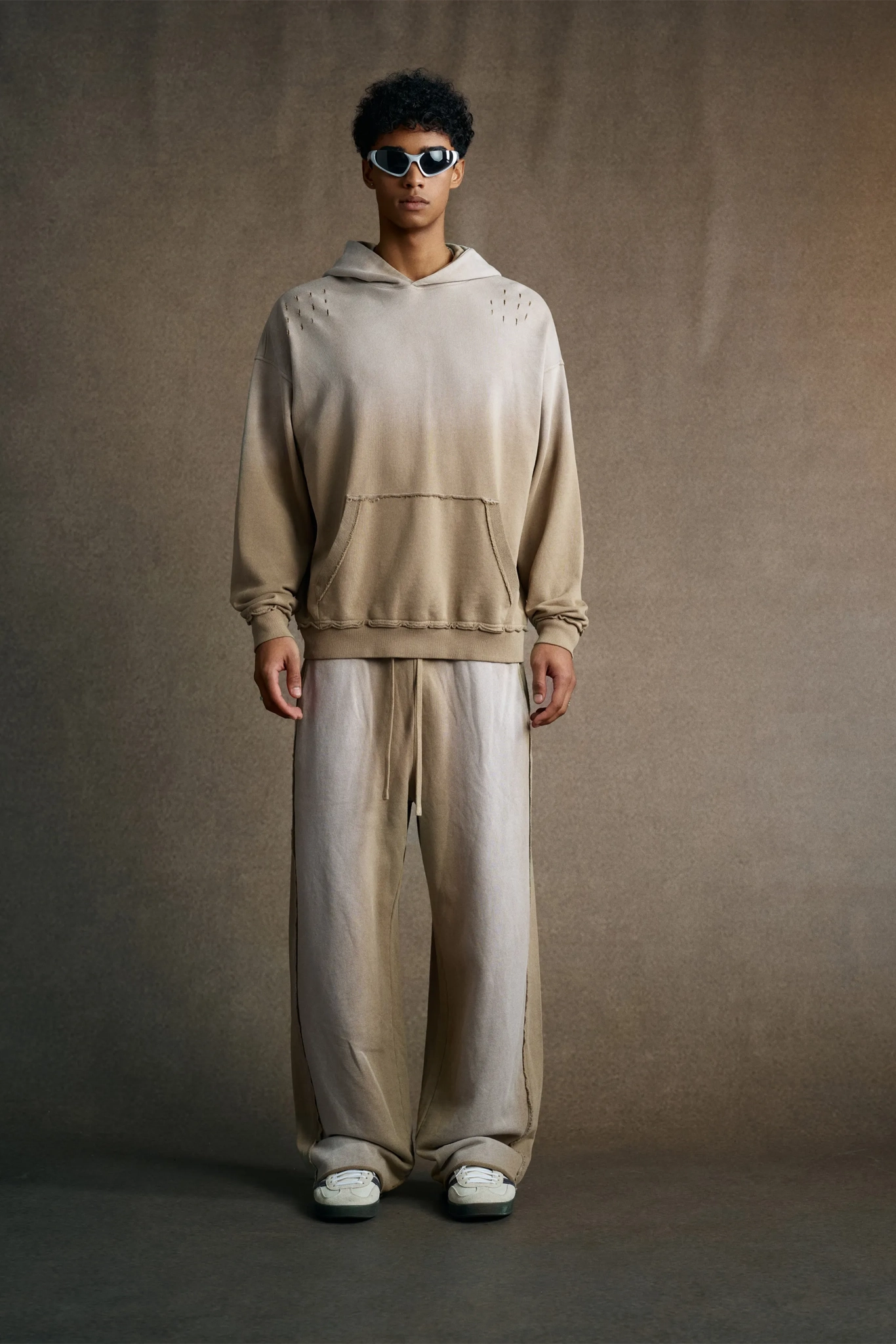 Person wearing a beige gradient hoodie and pants against a brown background