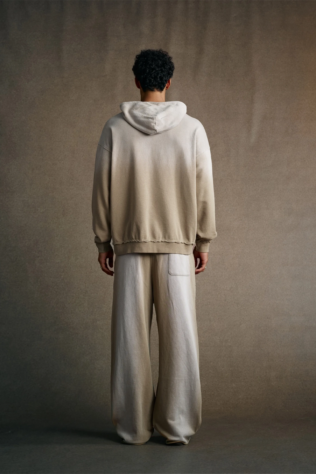 Person wearing a beige hoodie and pants against a plain background