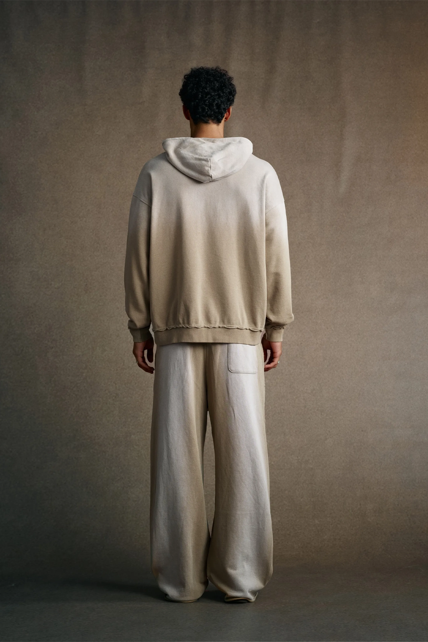 Person wearing a beige hoodie and pants against a plain background