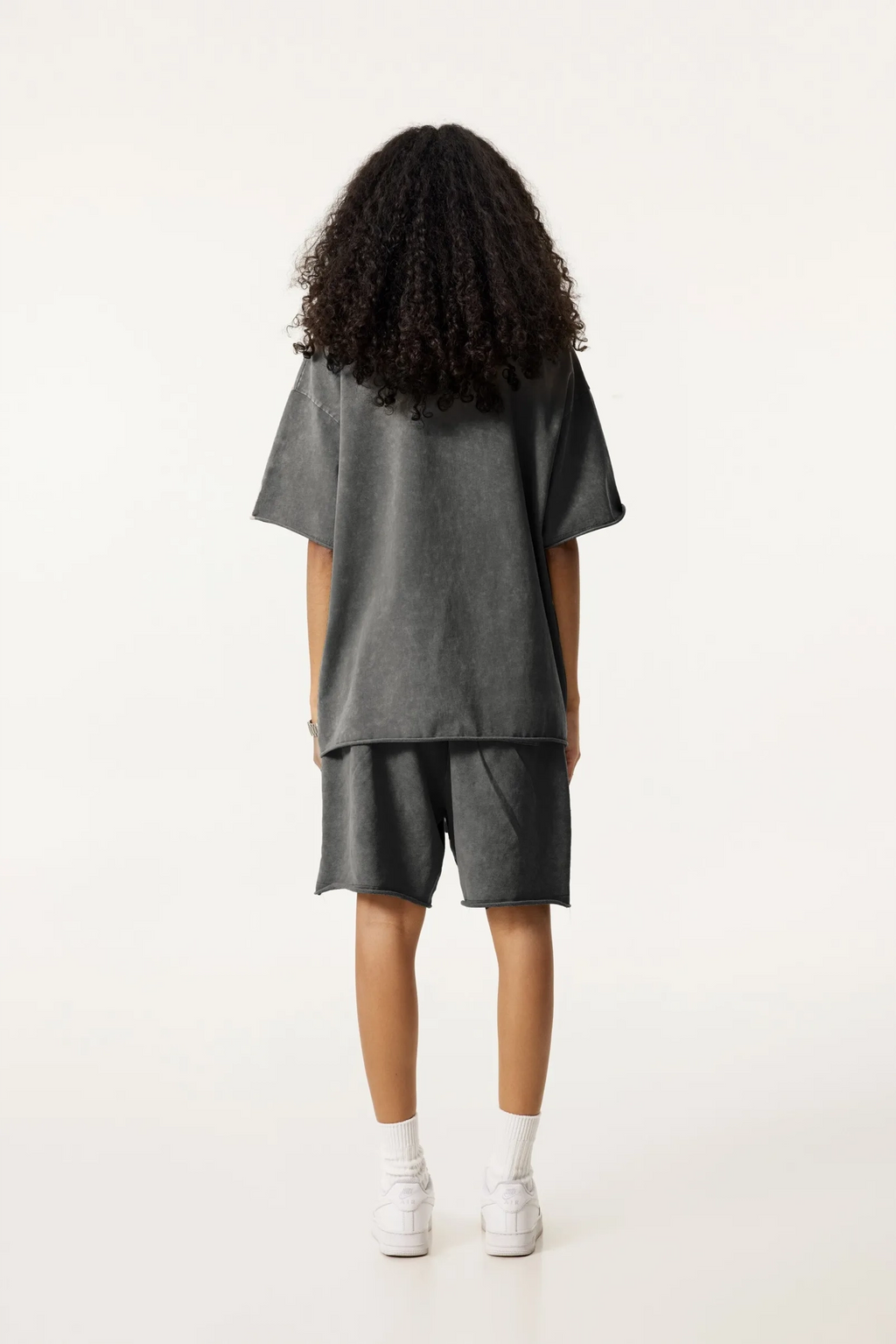 Person wearing a gray oversized t-shirt and shorts set on a white background
