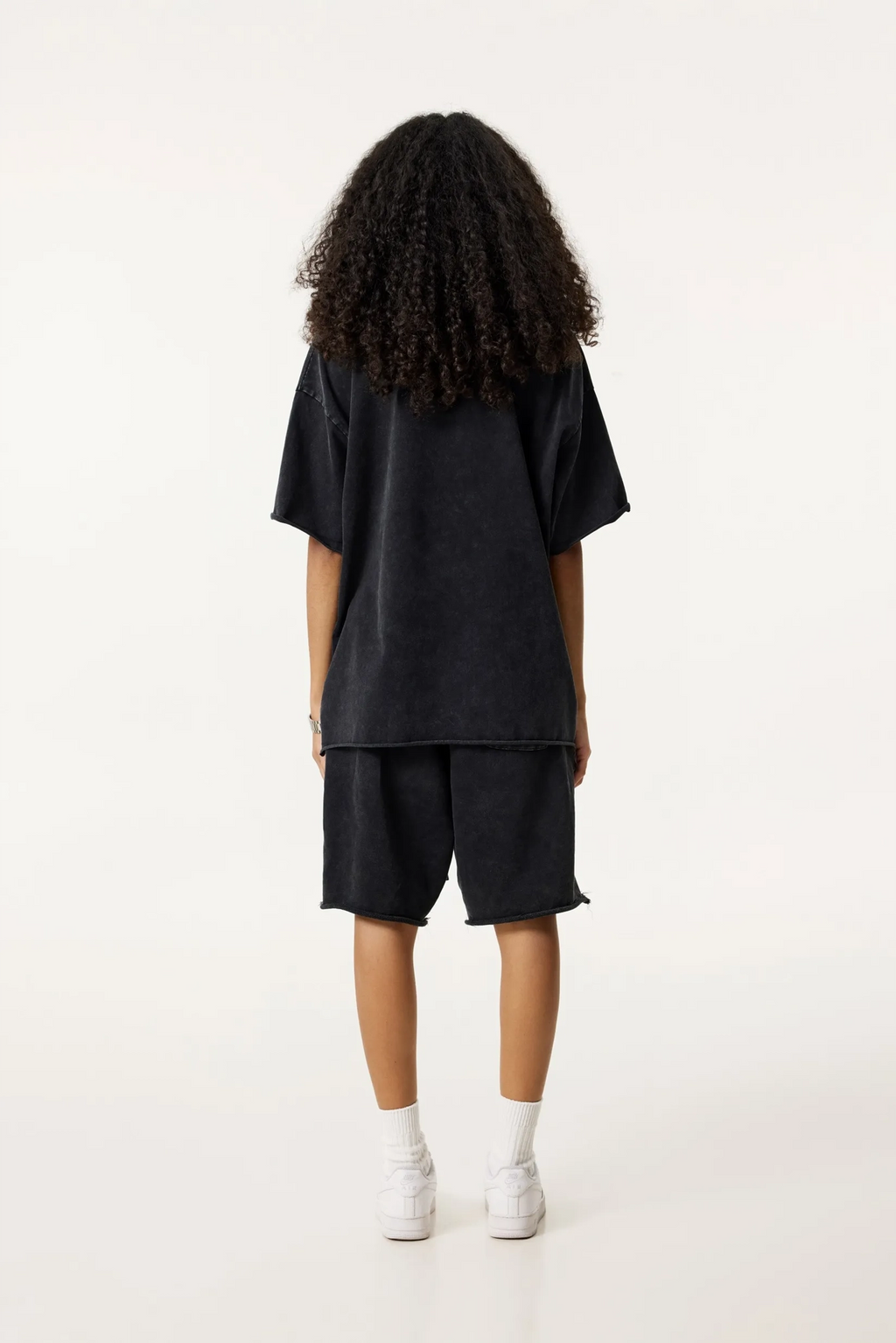 Person wearing a black oversized t-shirt and shorts set on a white background