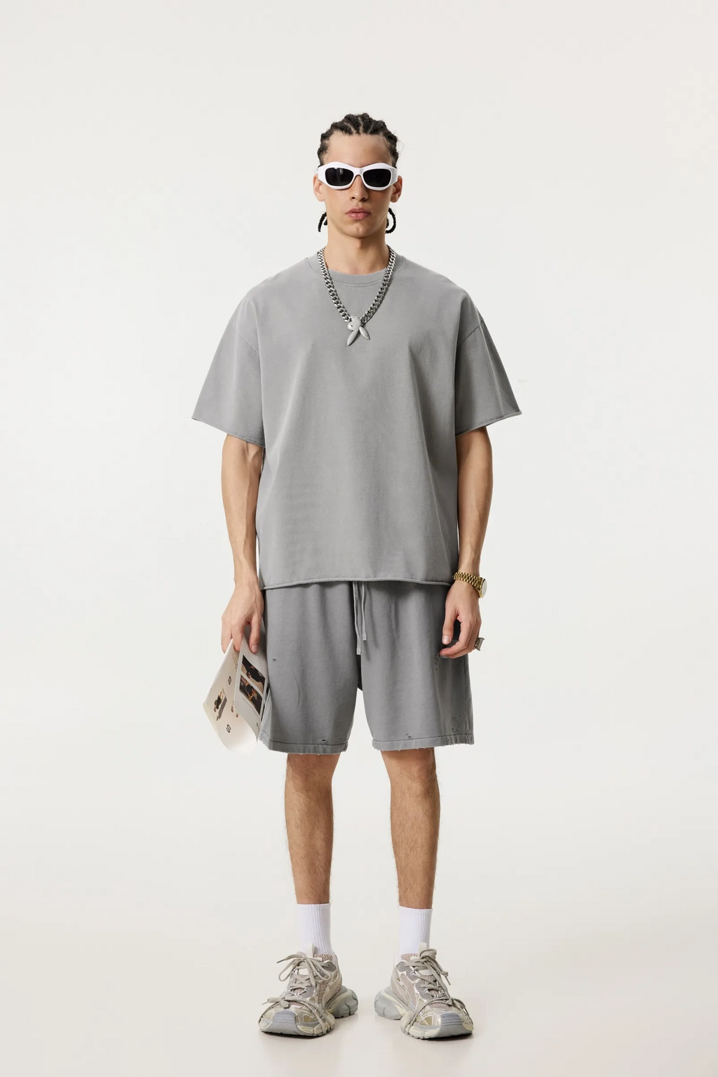 Person wearing a gray outfit with sunglasses and a necklace on a white background