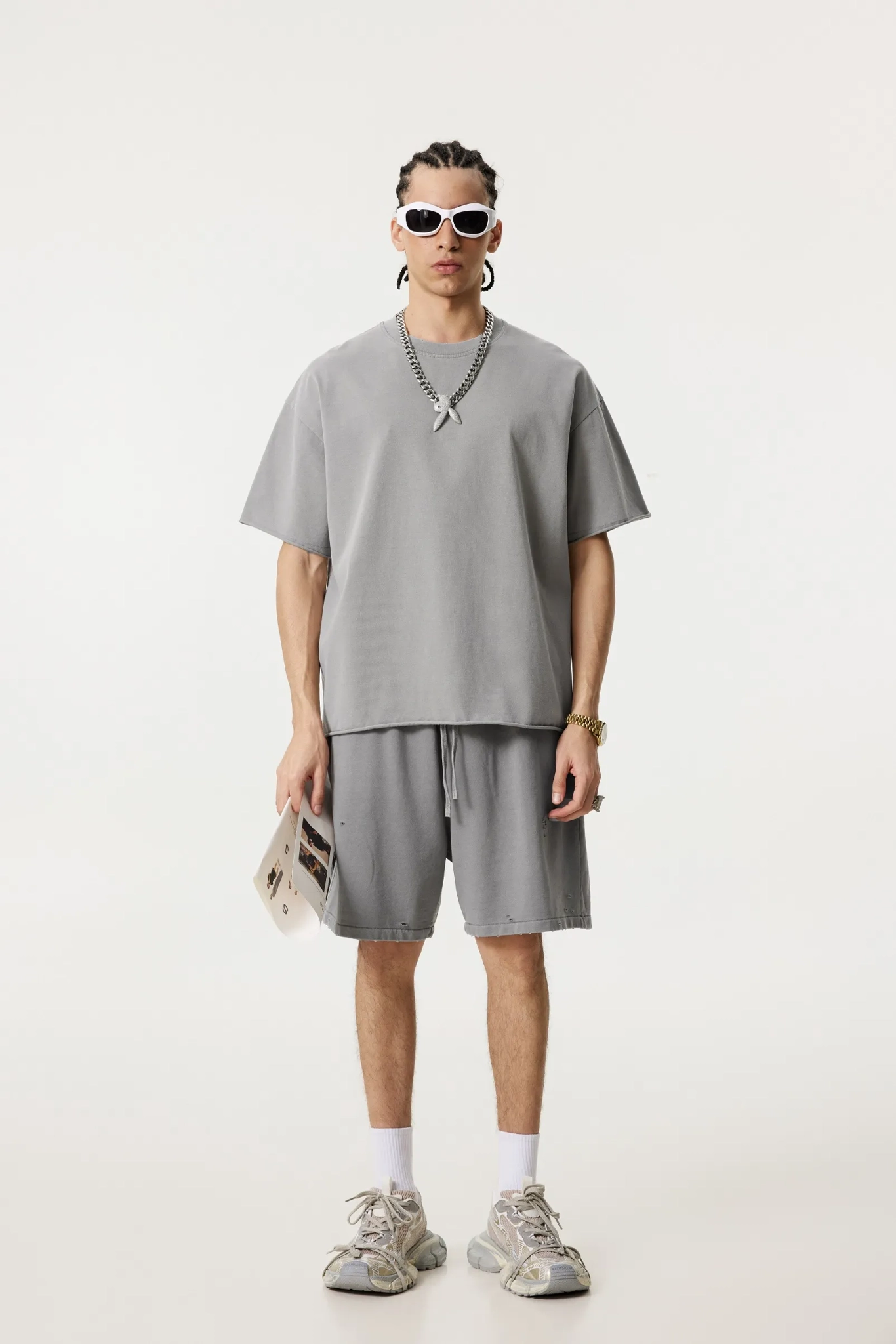 Person wearing a gray outfit with sunglasses and a necklace on a white background