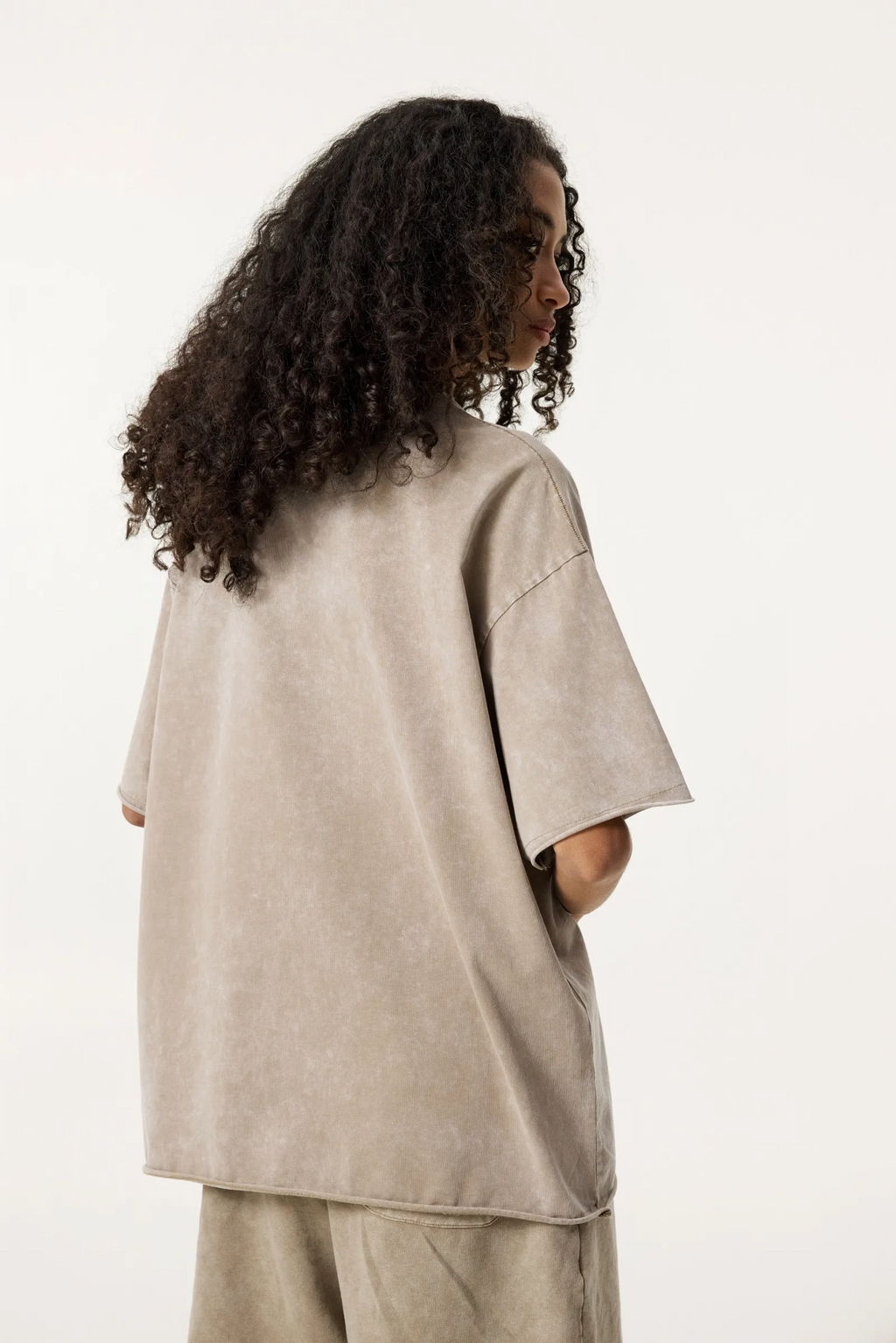 Person wearing a beige oversized shirt and pants on a white background