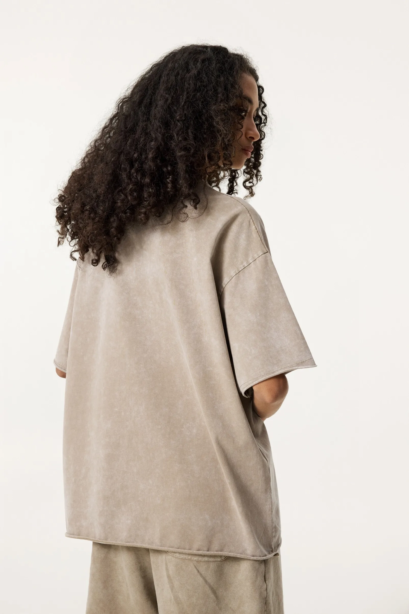 Person wearing a beige oversized shirt and pants on a white background