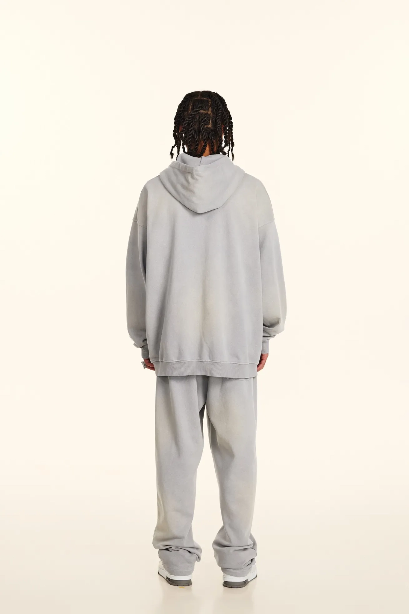 Person wearing a light gray hoodie and pants on a white background