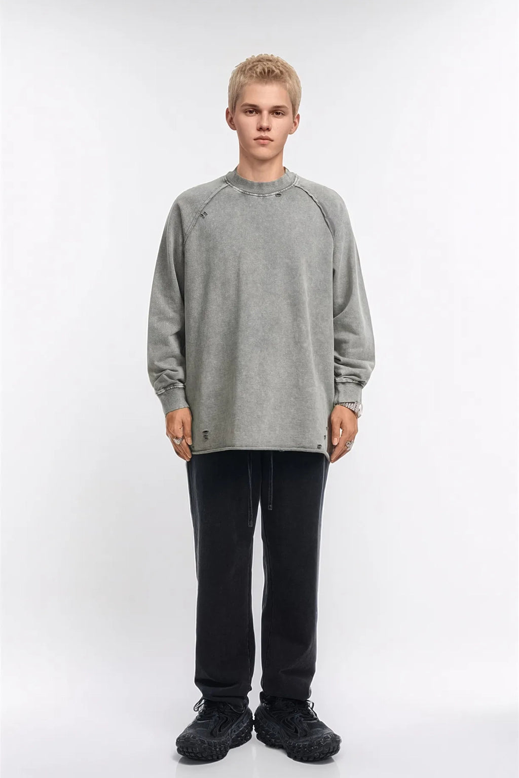 Person wearing a gray sweatshirt and black pants on a white background