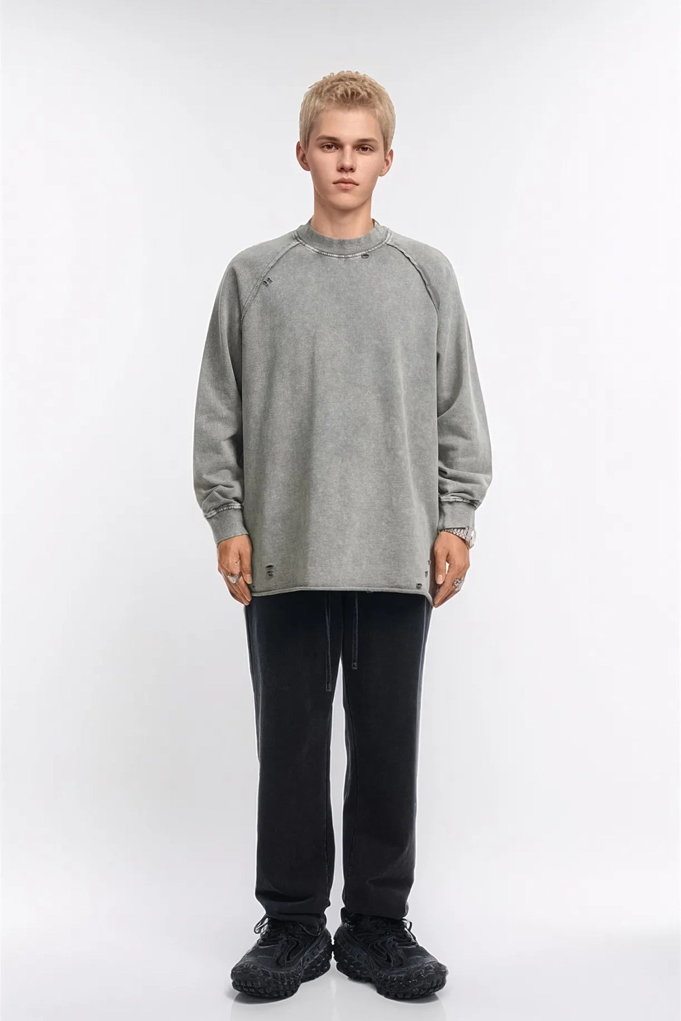 Person wearing a gray sweatshirt and black pants on a white background