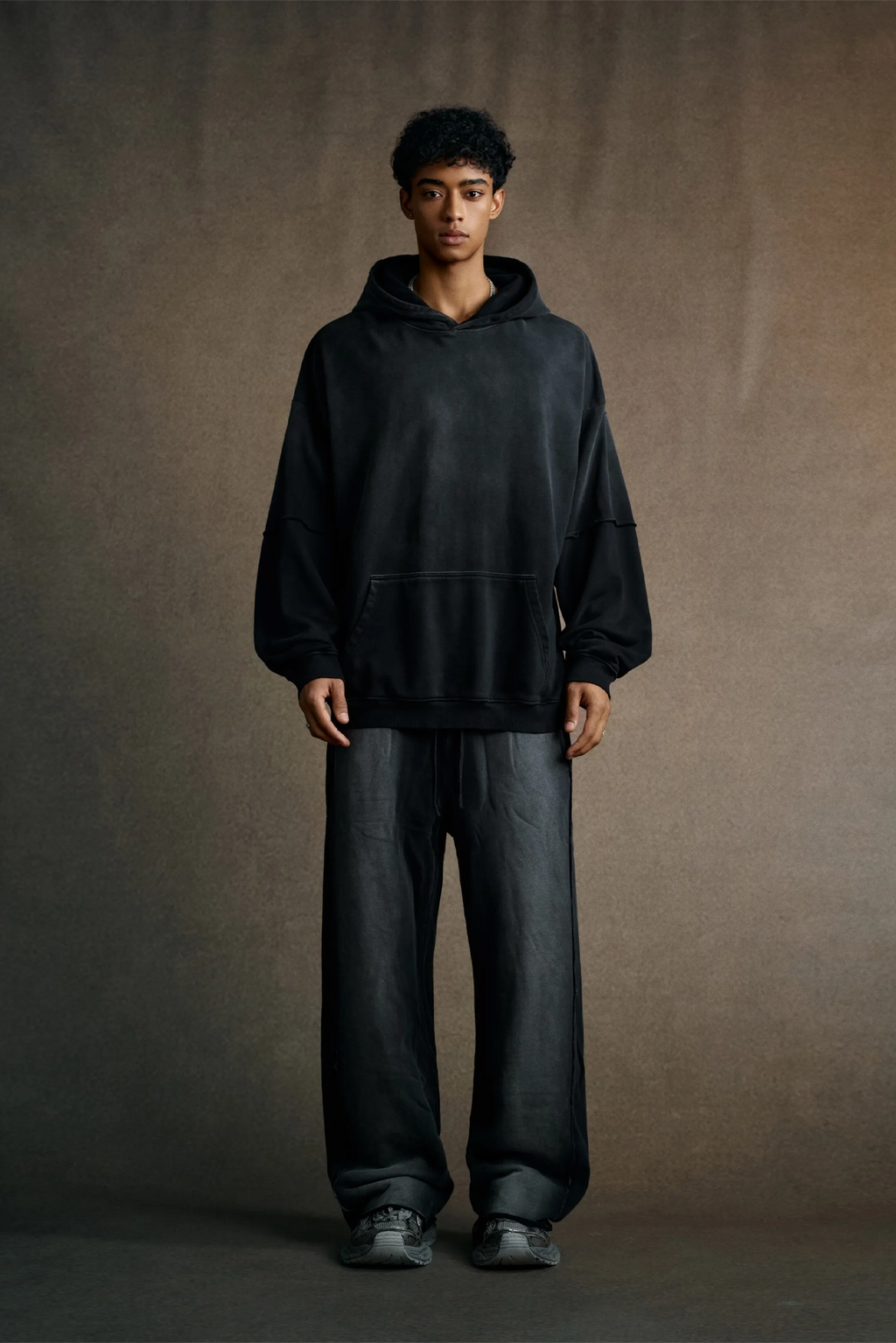Person wearing a black hoodie and pants against a brown background