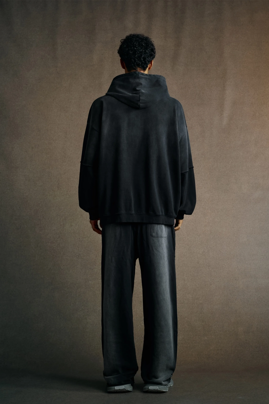 Person wearing a black hoodie and pants standing against a brown background